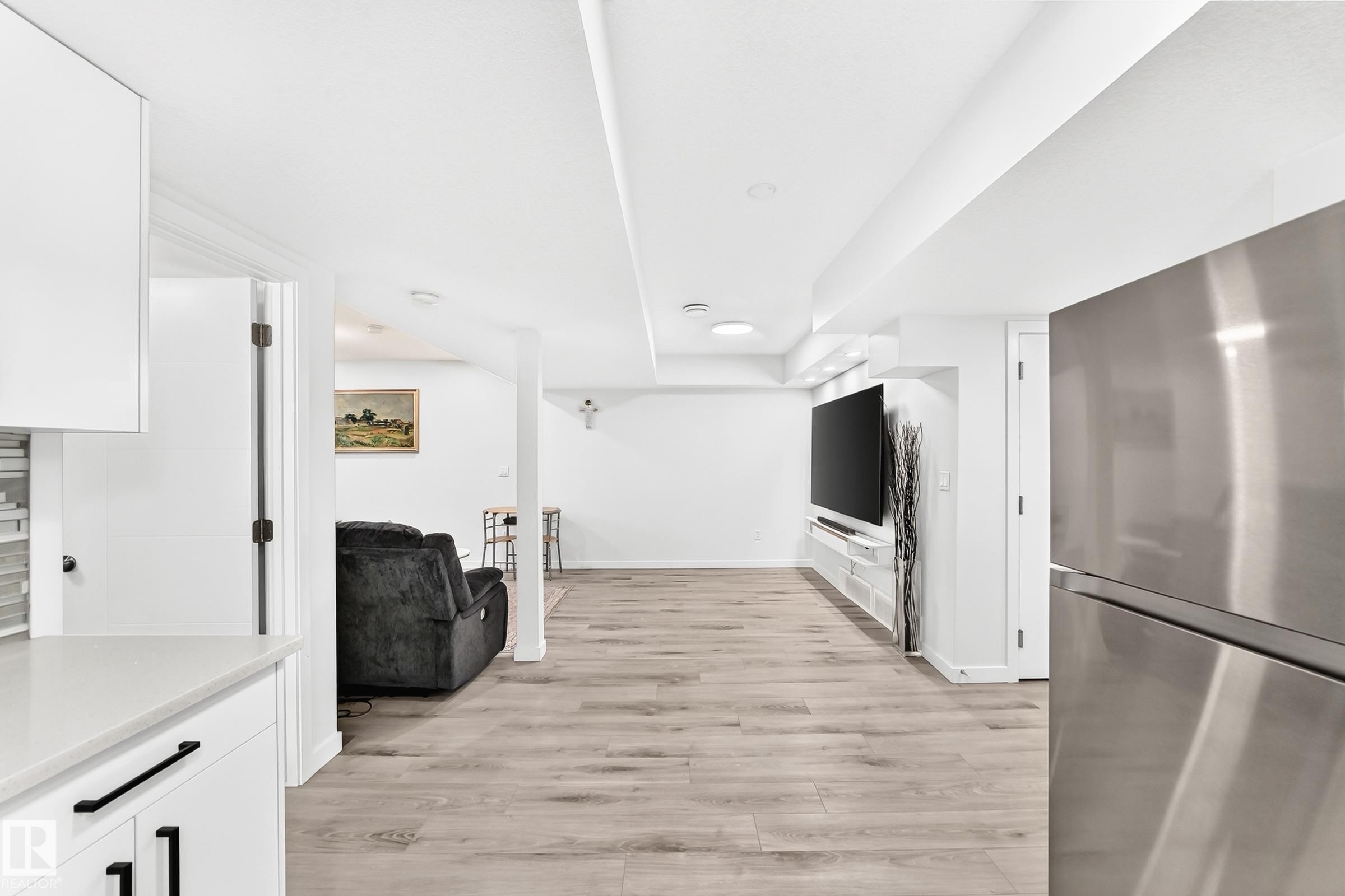 Open-concept lower level featuring recessed lighting, light wood-finish flooring, and a stainless steel refrigerator - 3672 Claxton Place Sw, Edmonton, AB