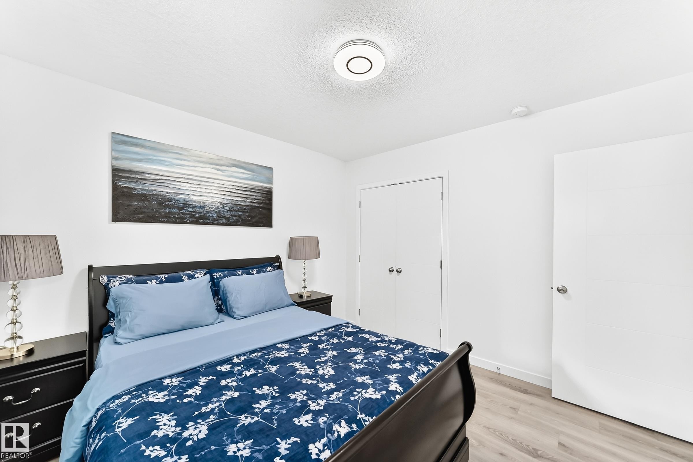 Bedroom featuring light wood-finish flooring, white walls, and a contemporary flush-mount ceiling light - 3672 Claxton Place Sw, Edmonton, AB