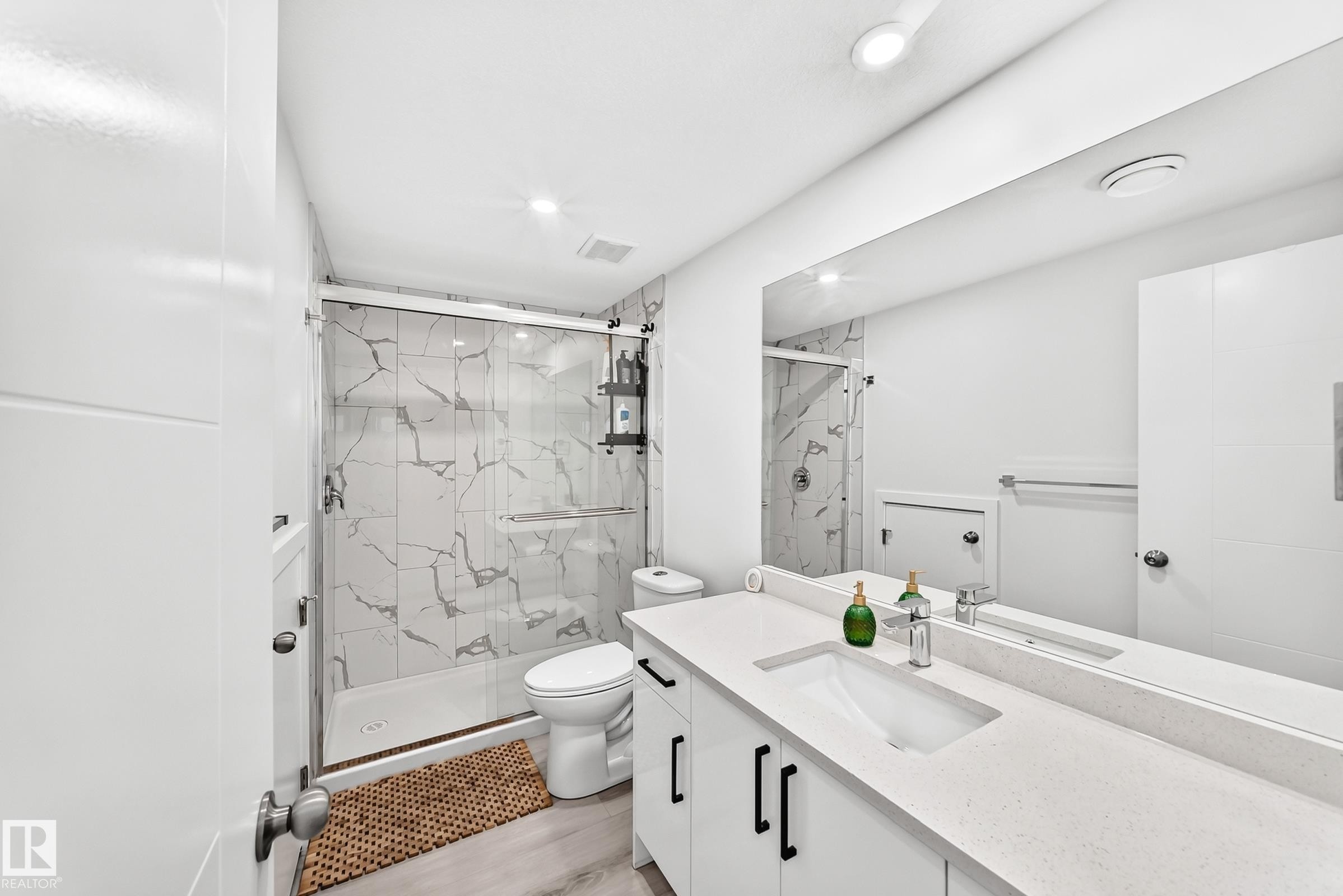 Contemporary bathroom featuring a spacious vanity with an integrated sink, a large mirror, and a walk-in shower with a glass enclosure and marble-look tile - 3672 Claxton Place Sw, Edmonton, AB