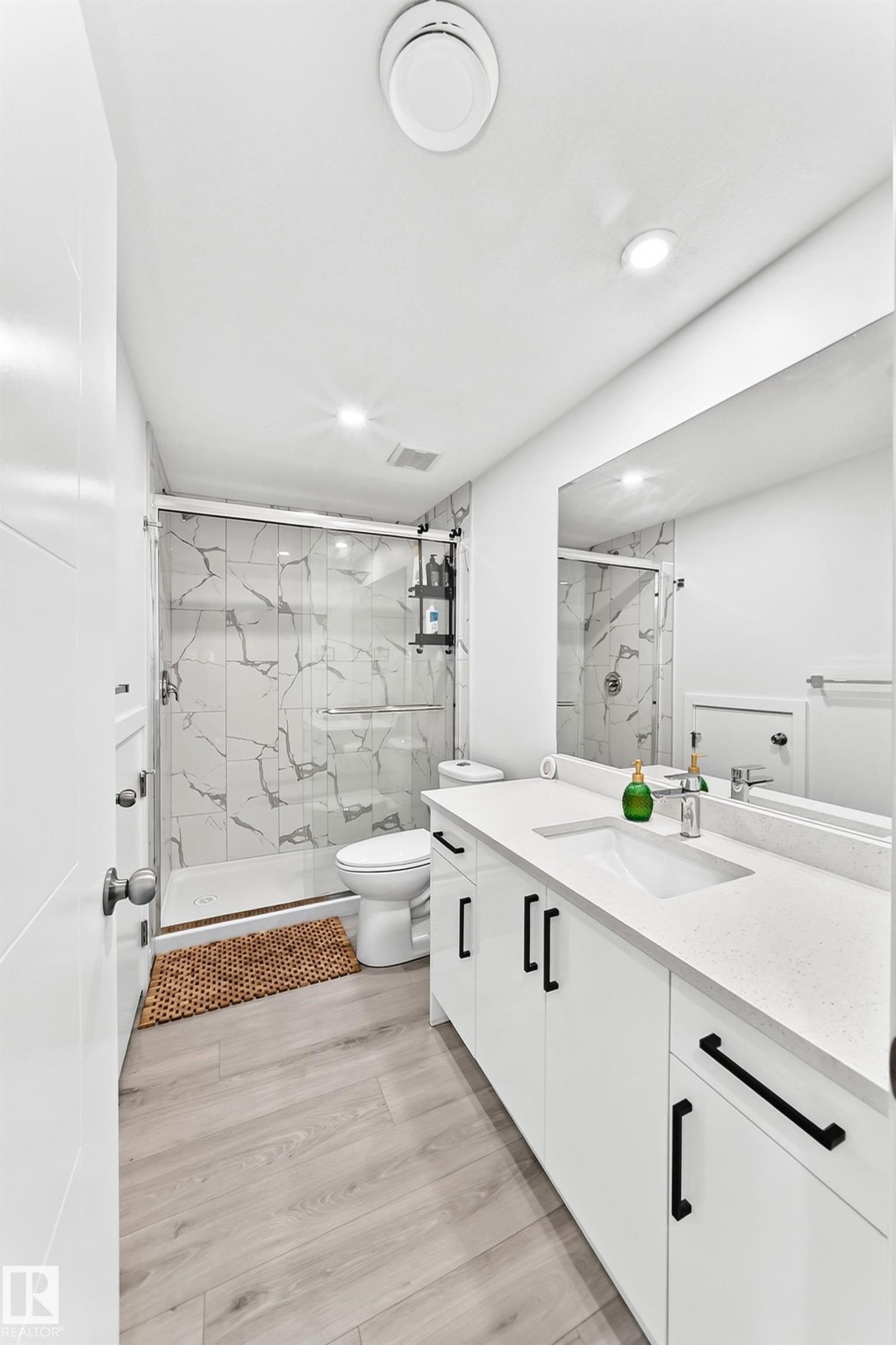 Bathroom featuring a dual vanity with white cabinetry and dark hardware, set against light wood-finish flooring - 3672 Claxton Place Sw, Edmonton, AB