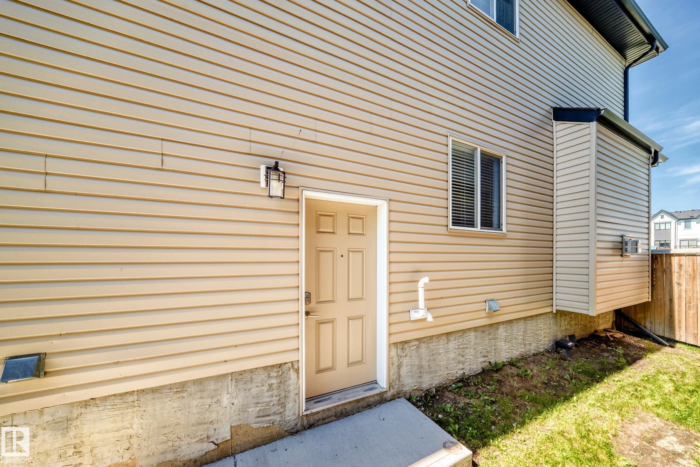 Exterior entry featuring beige horizontal siding, a paneled door, and an exterior wall lantern - 3672 Claxton Place Sw, Edmonton, AB