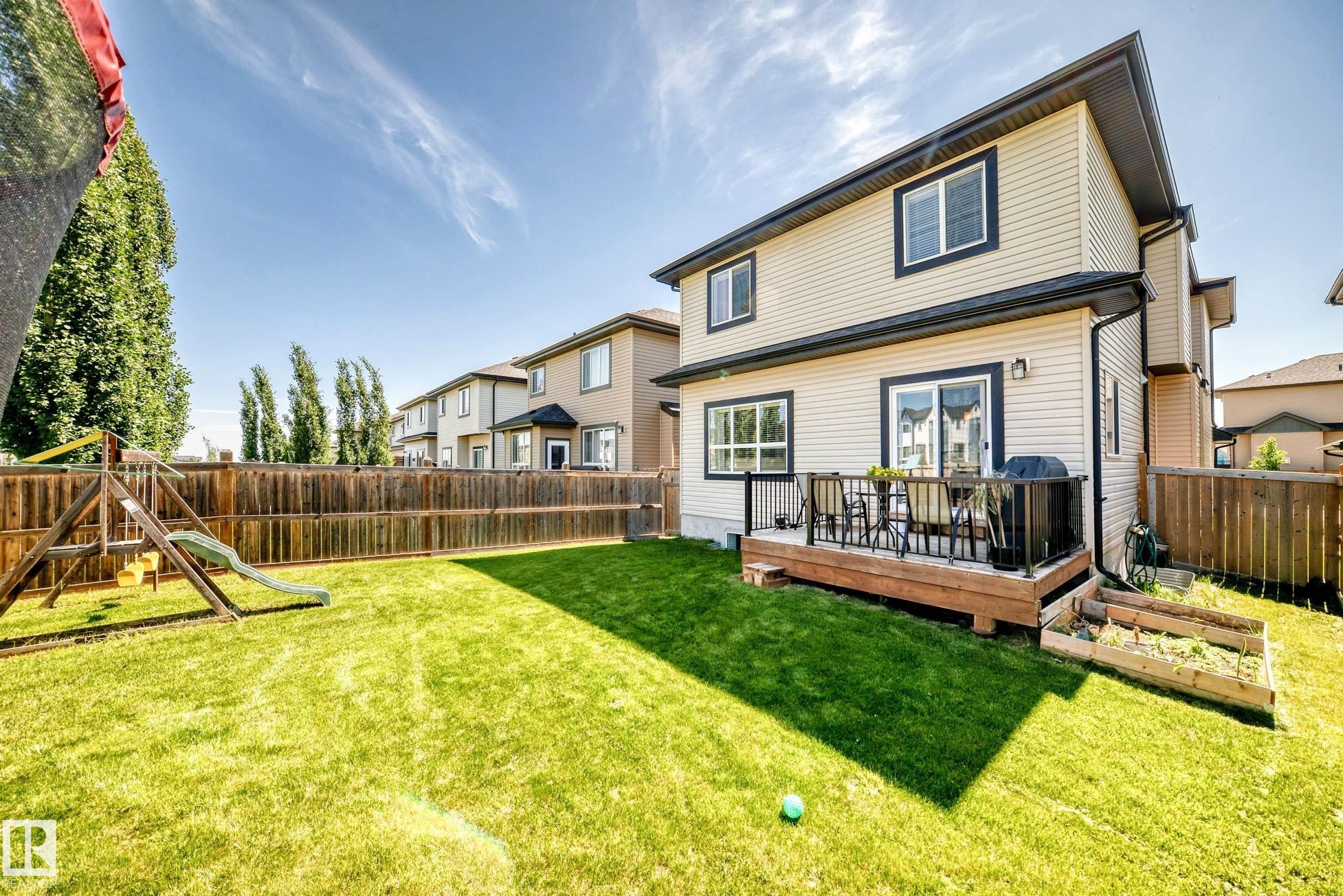 Spacious backyard featuring a manicured lawn, full wood privacy fencing, and a built-in wood deck with black metal railings - 3672 Claxton Place Sw, Edmonton, AB