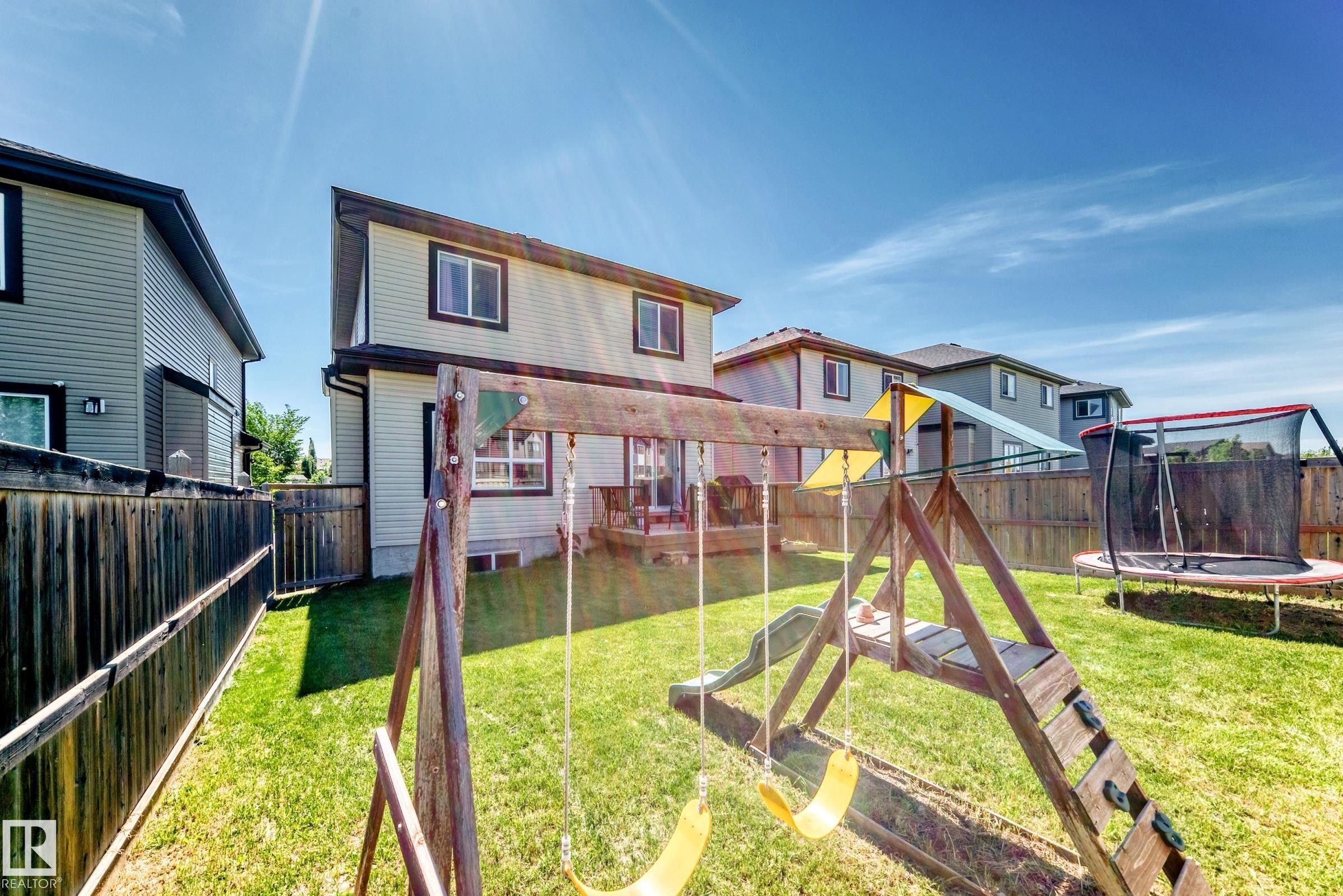 Expansive backyard featuring a manicured lawn, a wooden fence, and a two-story residence with a rear deck - 3672 Claxton Place Sw, Edmonton, AB