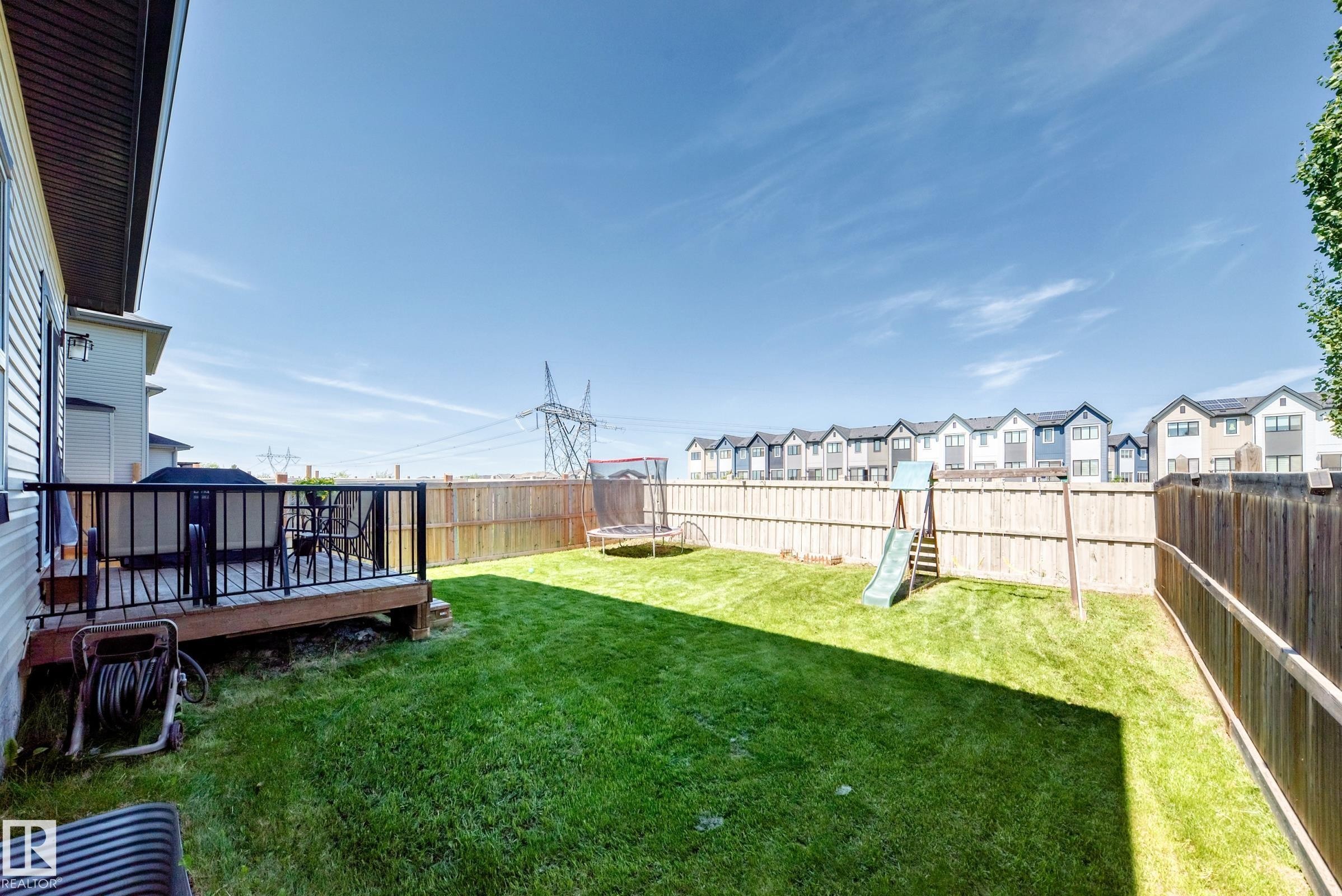 Expansive backyard featuring a green lawn, wood fence, and a raised wooden deck with black railings - 3672 Claxton Place Sw, Edmonton, AB