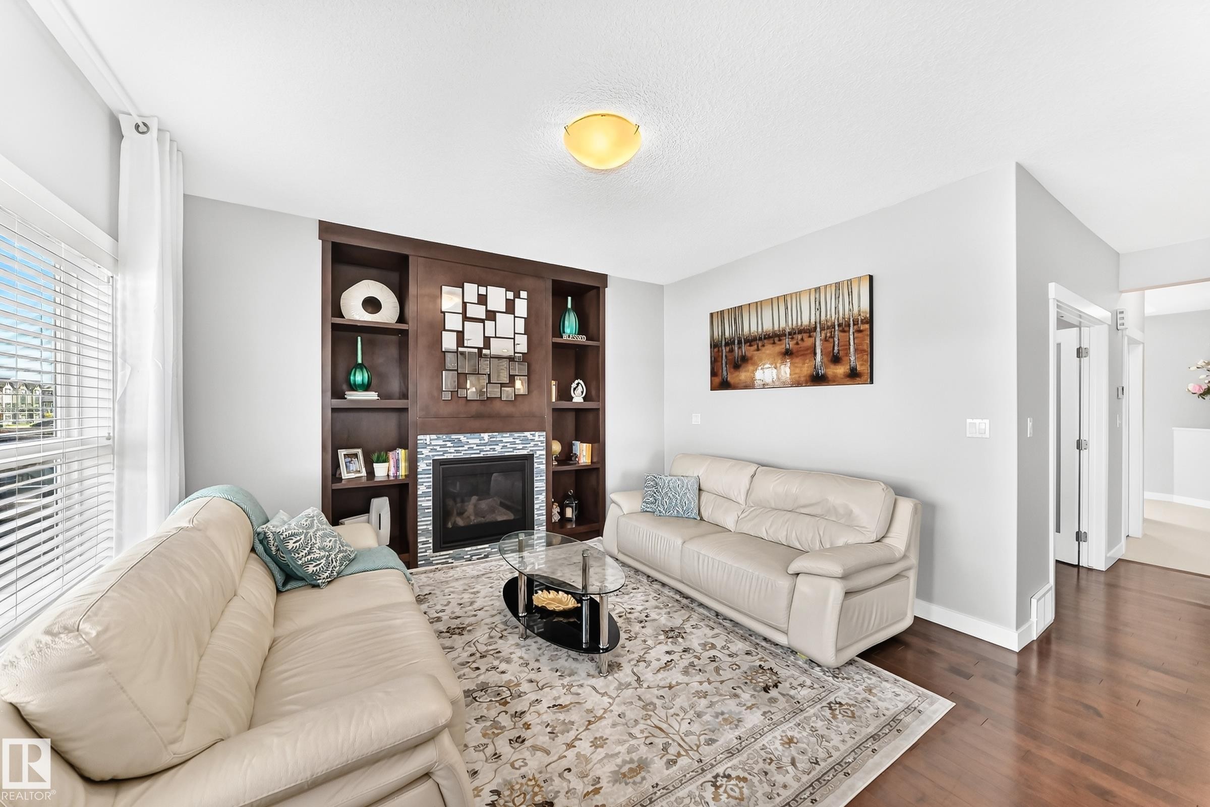 Living area featuring a built-in dark wood entertainment unit with shelving, a fireplace with a stone tile surround, and hardwood flooring - 3672 Claxton Place Sw, Edmonton, AB