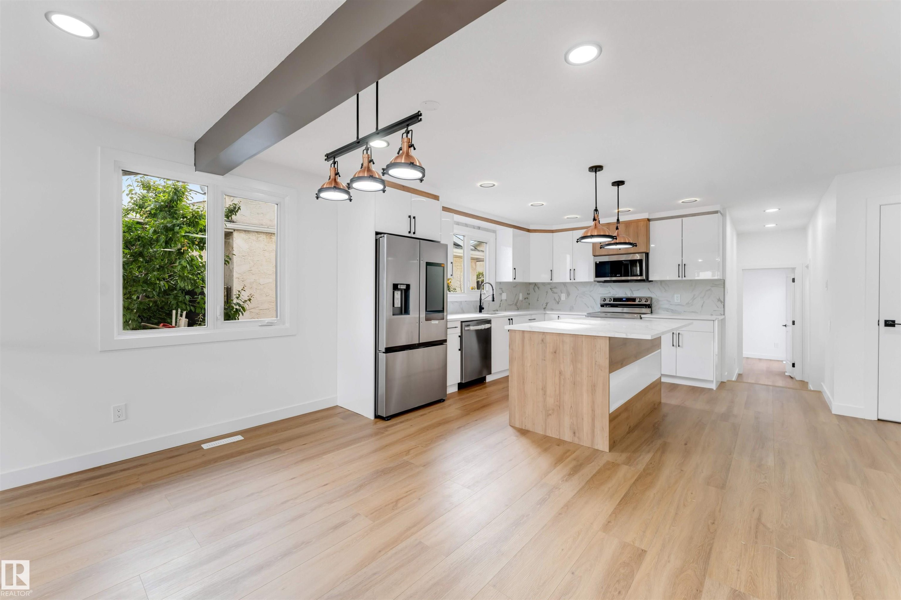 Open-concept kitchen and dining area featuring light wood-finish flooring, white cabinetry, stainless steel appliances, a central island with a quartz-finish countertop, and recessed lighting - 5512 150 Avenue, Edmonton, AB