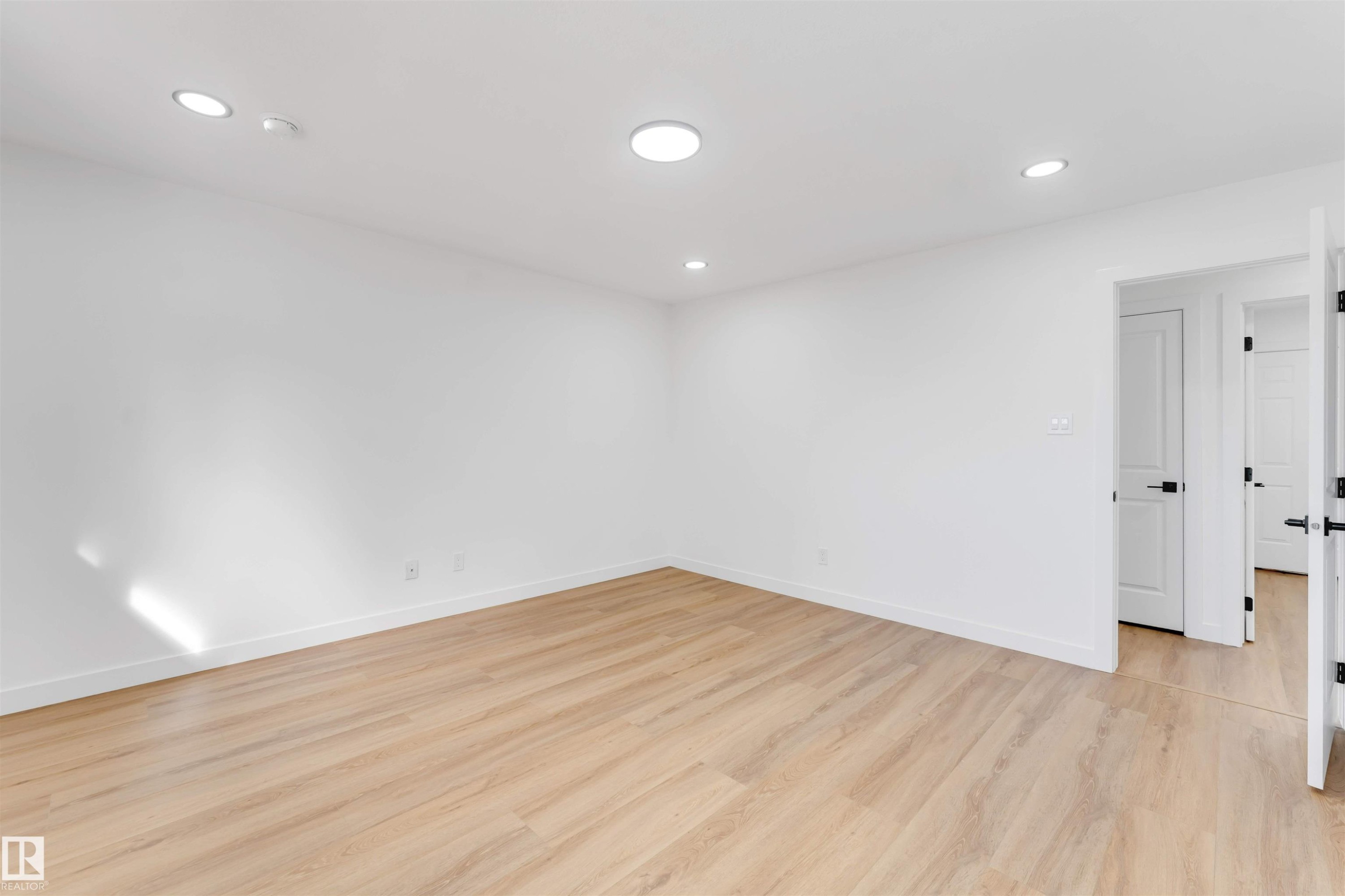 Bright interior space featuring light wood-finish flooring, recessed lighting, white baseboards, and white doors with matte black hardware - 5512 150 Avenue, Edmonton, AB