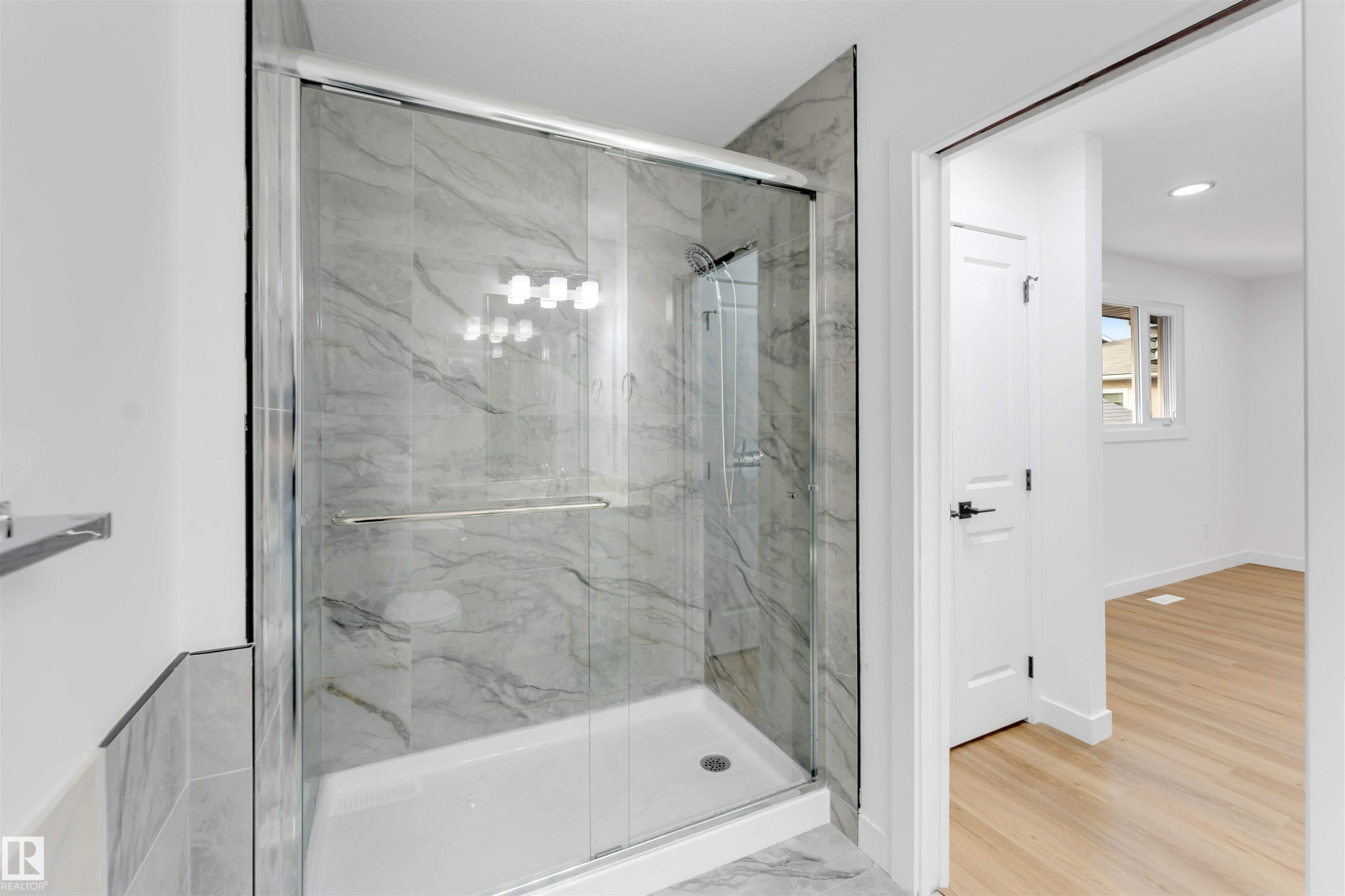 Glass-enclosed shower featuring large format veined wall tiling, a chrome showerhead, and a white shower pan - 5512 150 Avenue, Edmonton, AB