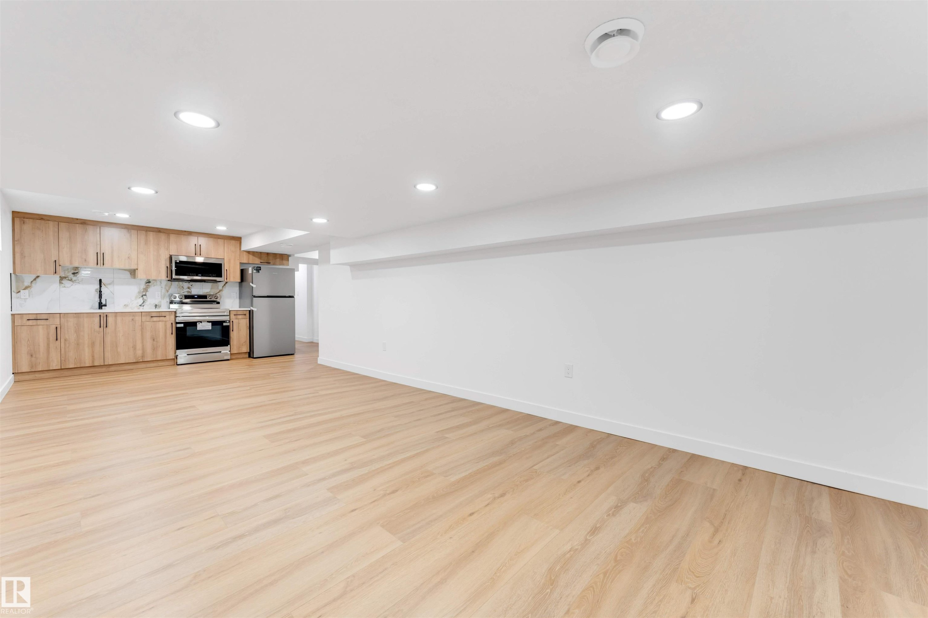 Open-concept living space featuring wood-finish flooring, recessed lighting, and a kitchen with stainless steel appliances, light wood cabinetry, and a patterned backsplash - 5512 150 Avenue, Edmonton, AB
