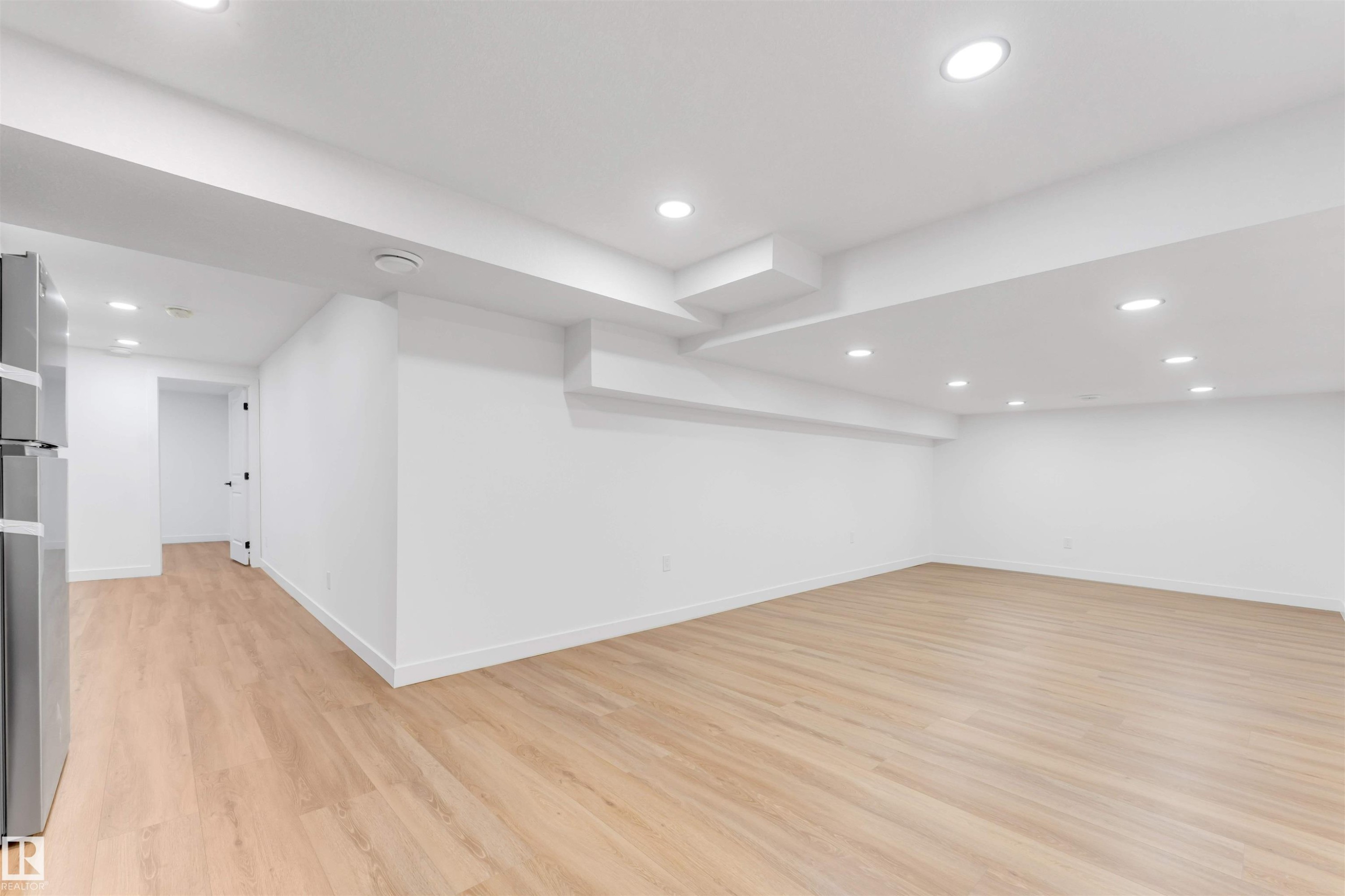 Spacious room featuring light wood-finish flooring, recessed ceiling lighting, white walls, and white baseboards - 5512 150 Avenue, Edmonton, AB