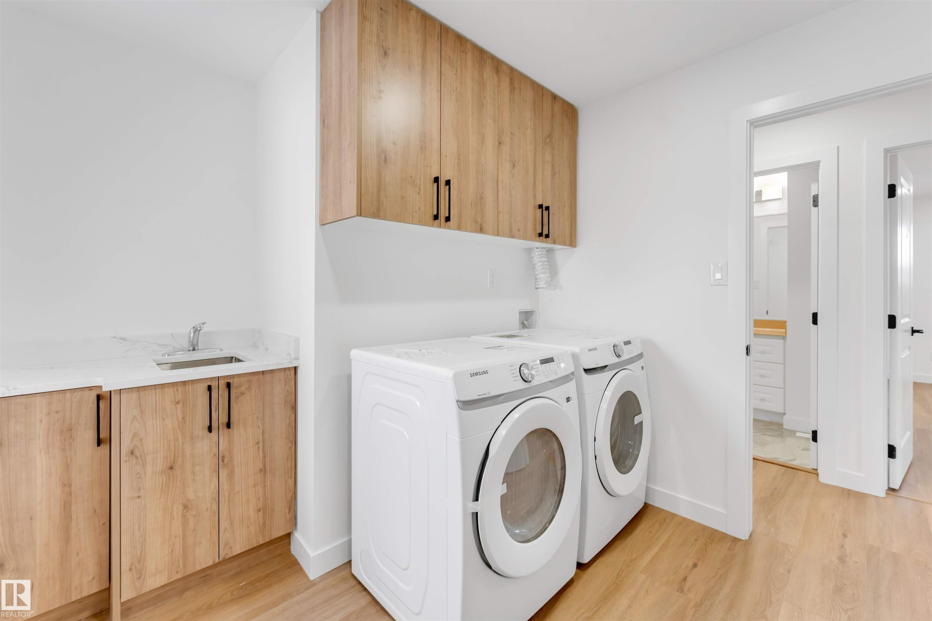 Utility room featuring wood-finish cabinetry, a white countertop with an undermount sink, and light wood-finish flooring - 5512 150 Avenue, Edmonton, AB