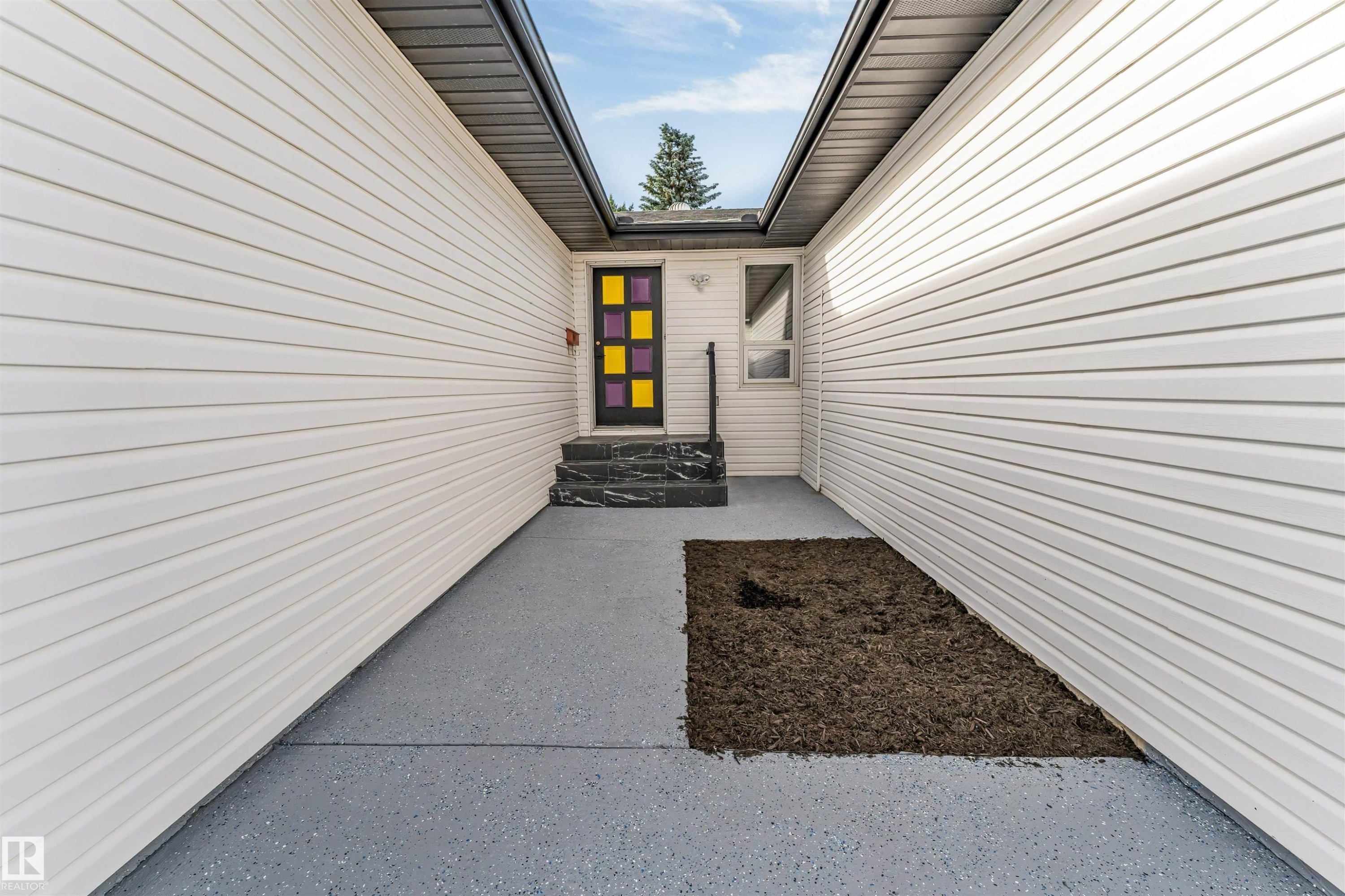 Covered entryway featuring light-toned horizontal siding, a dark framed door with colorful paneled inserts, and dark patterned steps - 5512 150 Avenue, Edmonton, AB