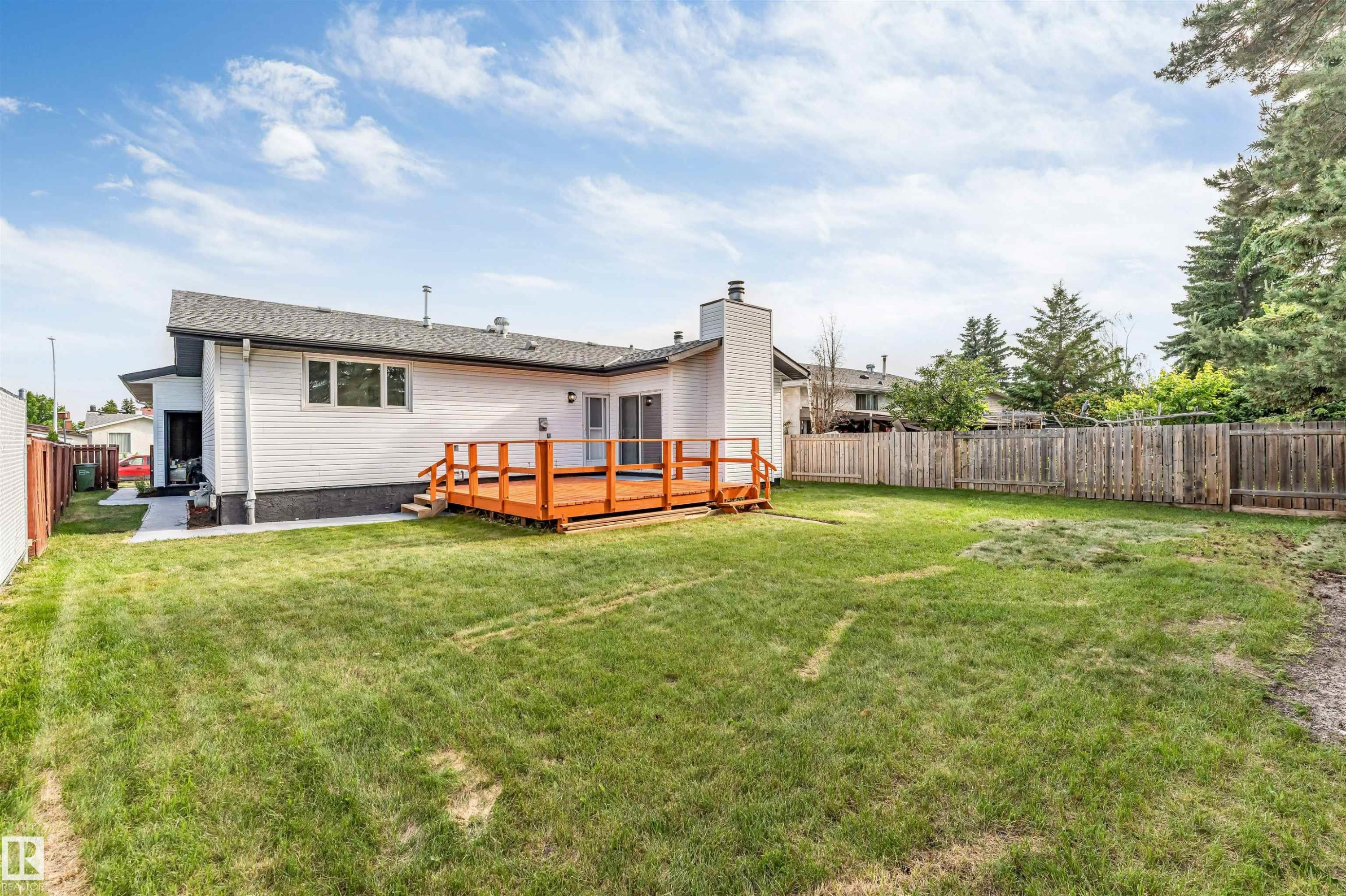 Expansive grass lawn with a wood deck, wood privacy fence, and concrete pathway - 5512 150 Avenue, Edmonton, AB