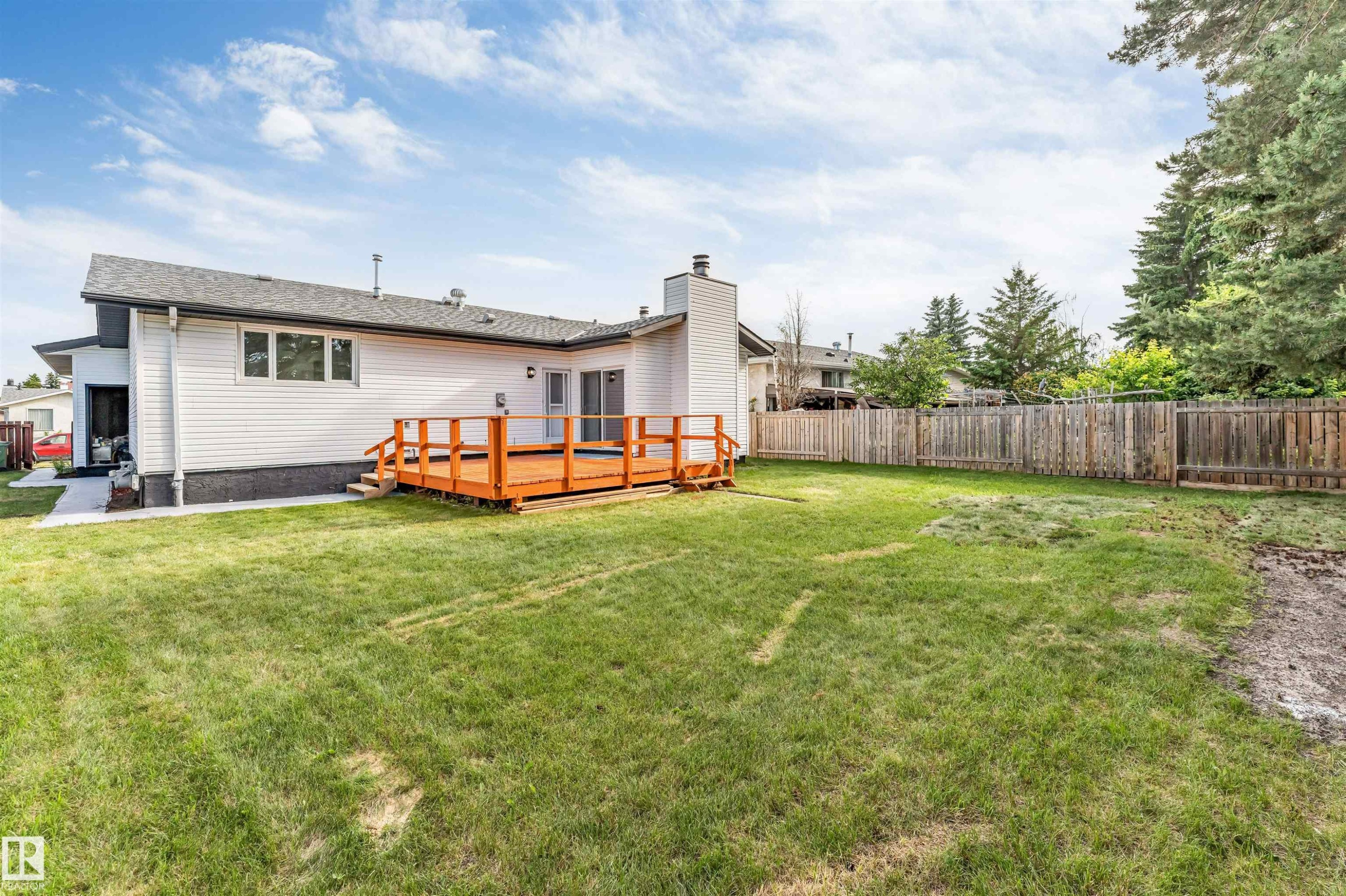 Expansive backyard featuring a stained wood deck, a perimeter wood fence, and mature evergreen trees - 5512 150 Avenue, Edmonton, AB