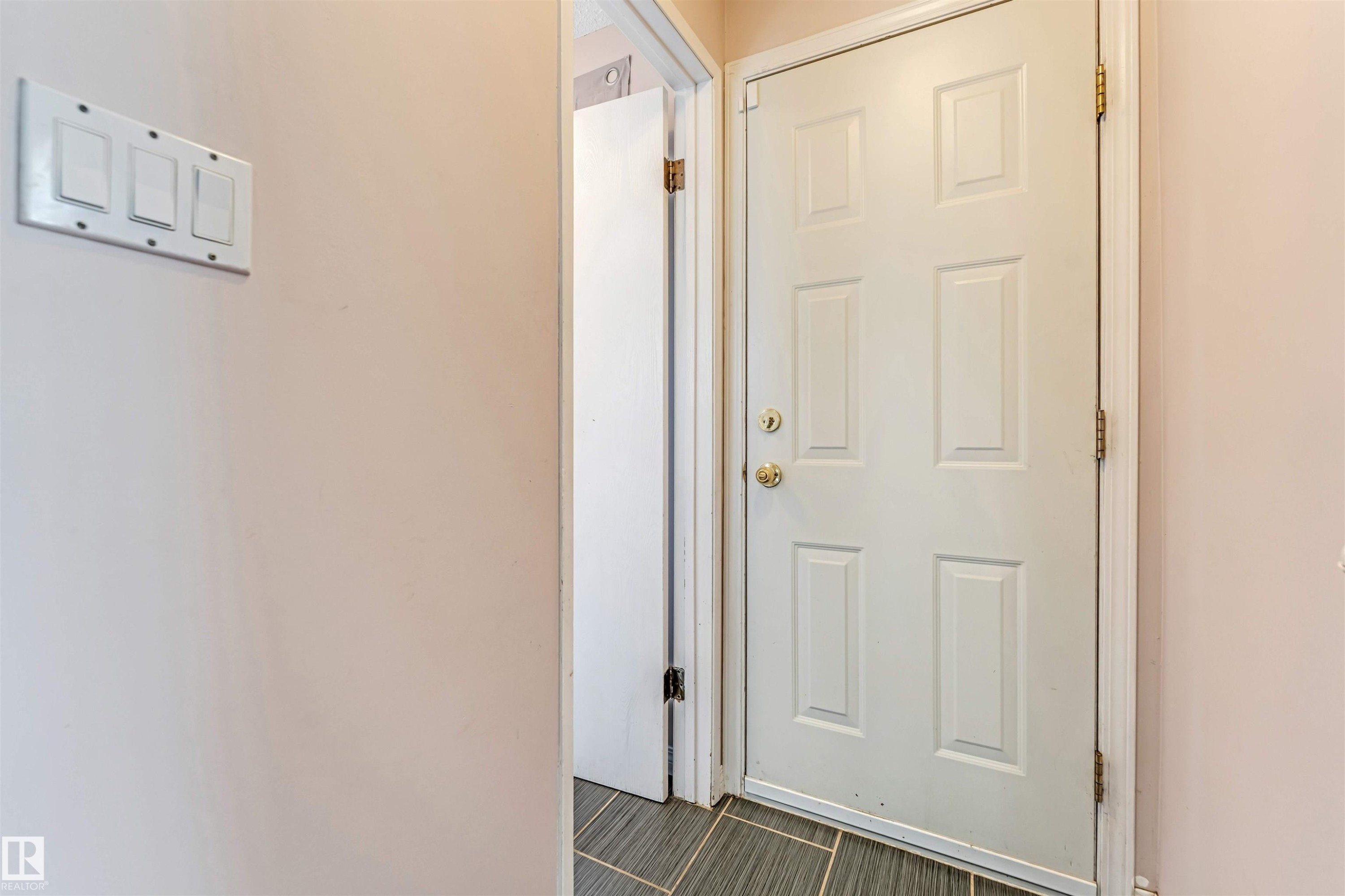 White paneled door with brass hardware, complemented by light-toned wall paint and dark gray tile flooring - 24 1651 46 Street, Edmonton, AB