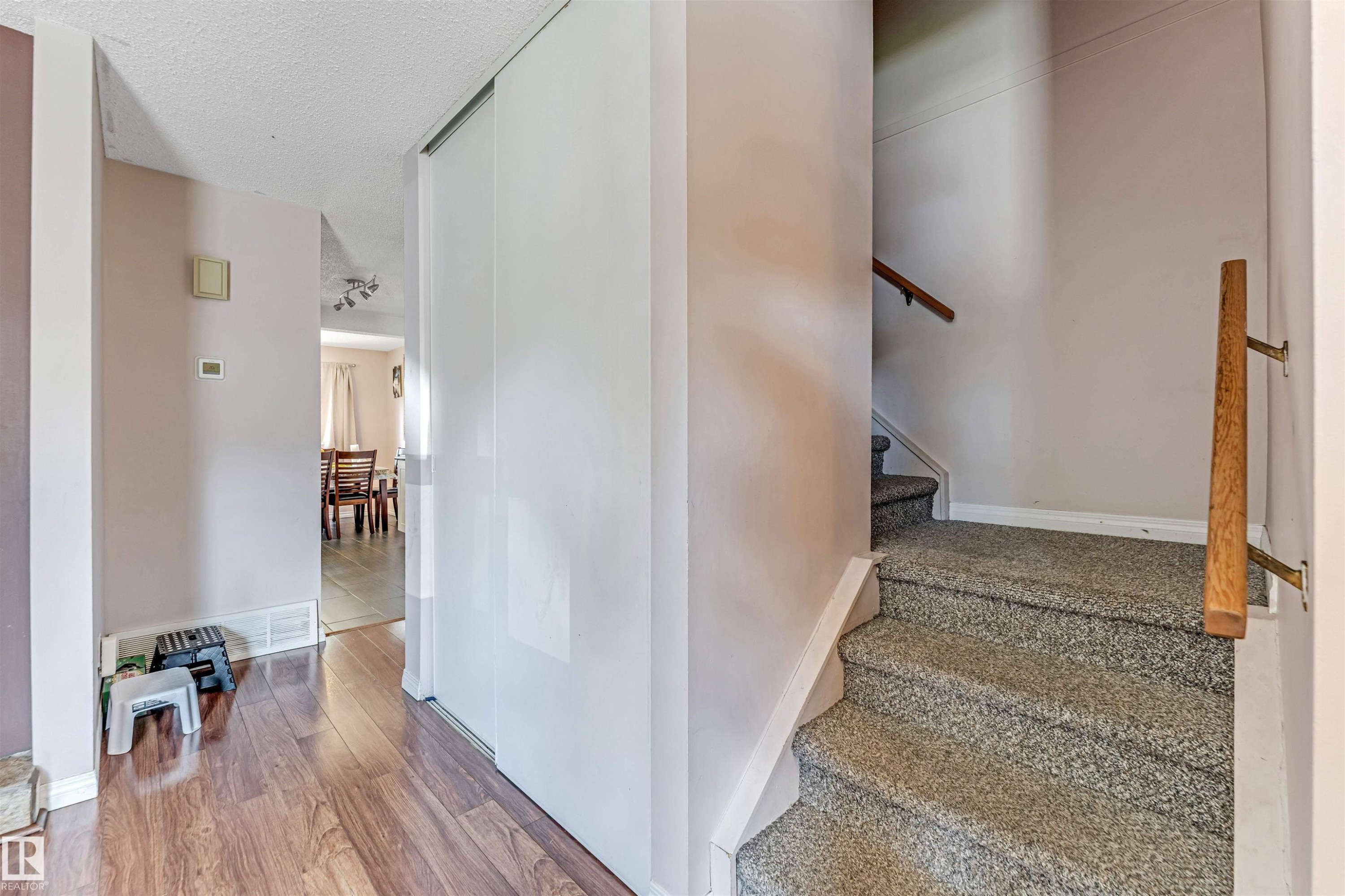 Entryway featuring wood-finish flooring, a full-height sliding closet, and a carpeted staircase with a wood handrail - 24 1651 46 Street, Edmonton, AB