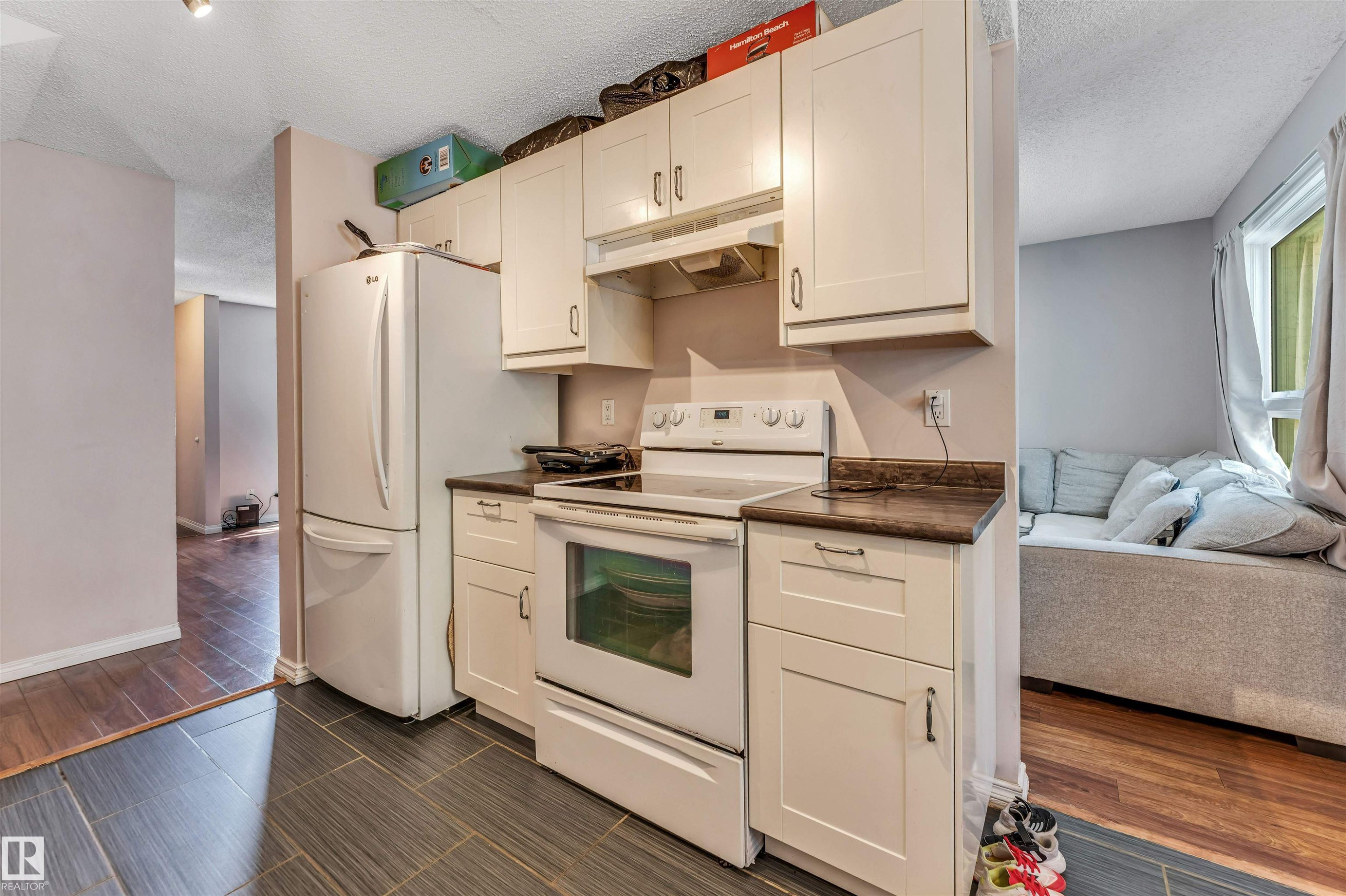 Kitchen featuring white cabinetry with brushed nickel hardware, a white electric range with overhead hood, a white refrigerator, and dark wood-finish countertops - 24 1651 46 Street, Edmonton, AB