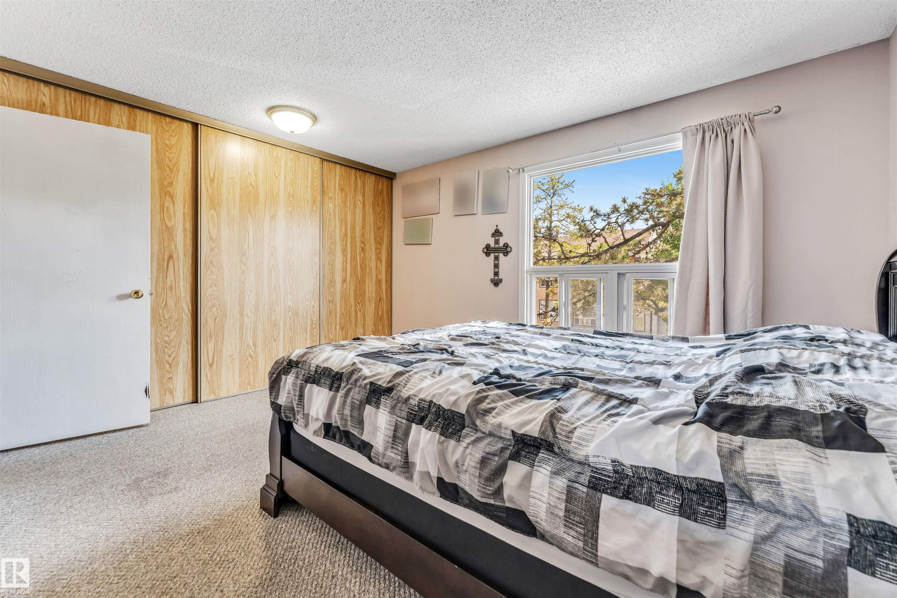 Bright room featuring light-toned carpeting, a window with exterior tree scenery, and wood-finish sliding closet doors - 24 1651 46 Street, Edmonton, AB