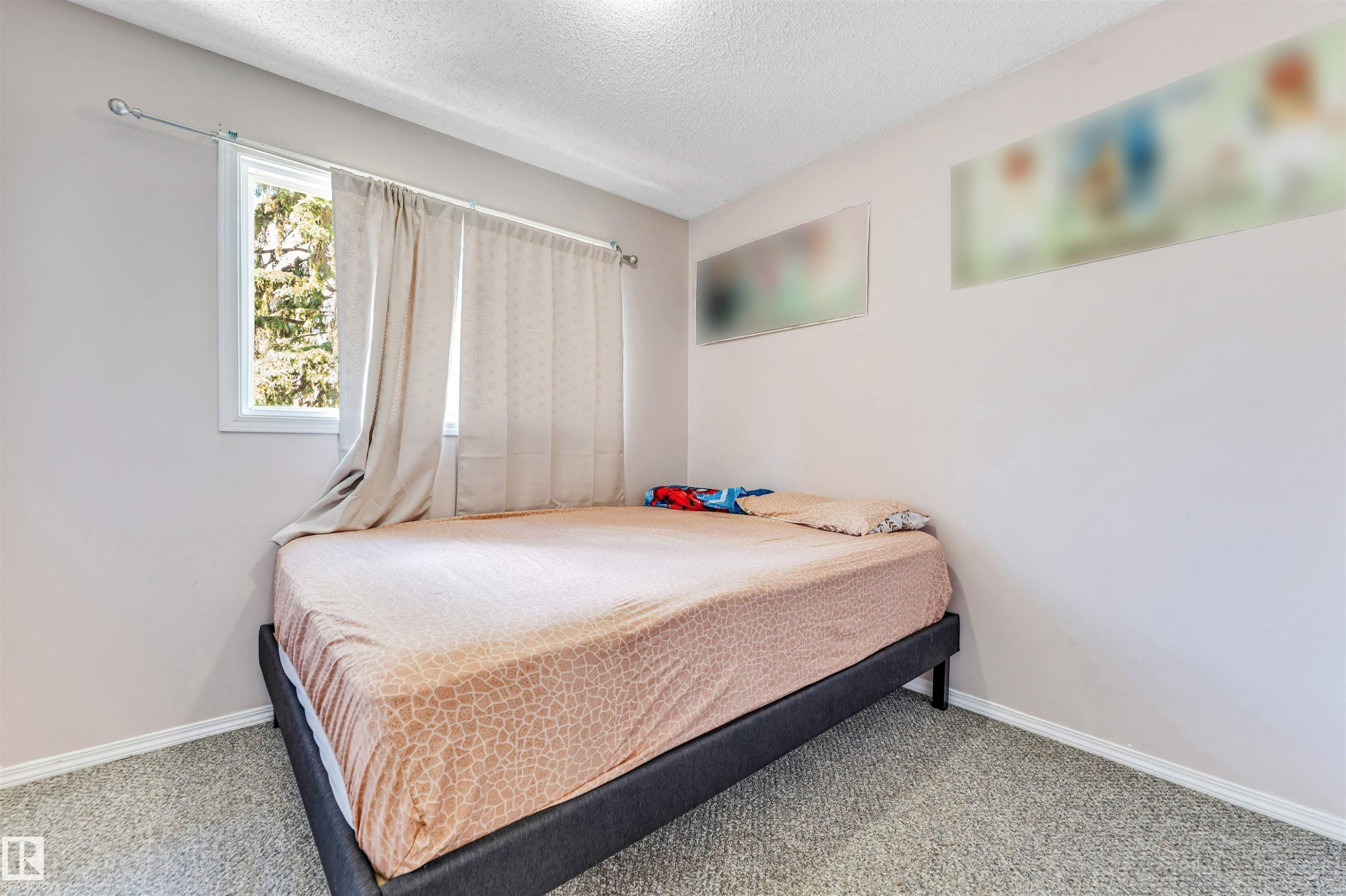 Bedroom featuring a window with exterior tree scenery, light-colored walls, and textured carpeting - 24 1651 46 Street, Edmonton, AB