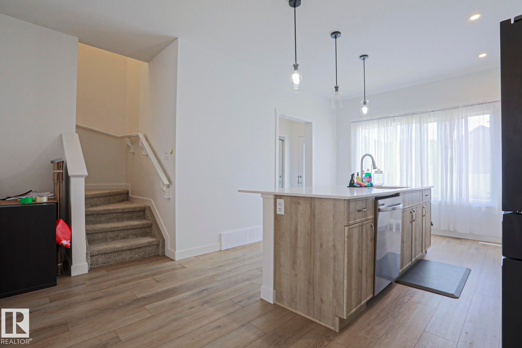 Kitchen island featuring a sink with a gooseneck faucet, integrated dishwasher, and wood-finish cabinetry - 33 Eton Link, Spruce Grove, AB