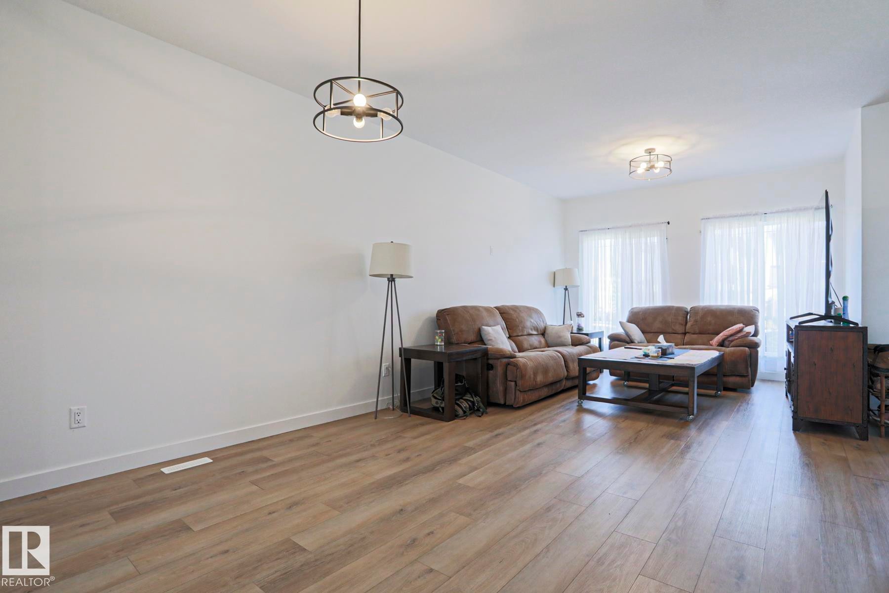 Spacious living area featuring light wood-finish flooring, white walls, and a modern circular chandelier - 33 Eton Link, Spruce Grove, AB