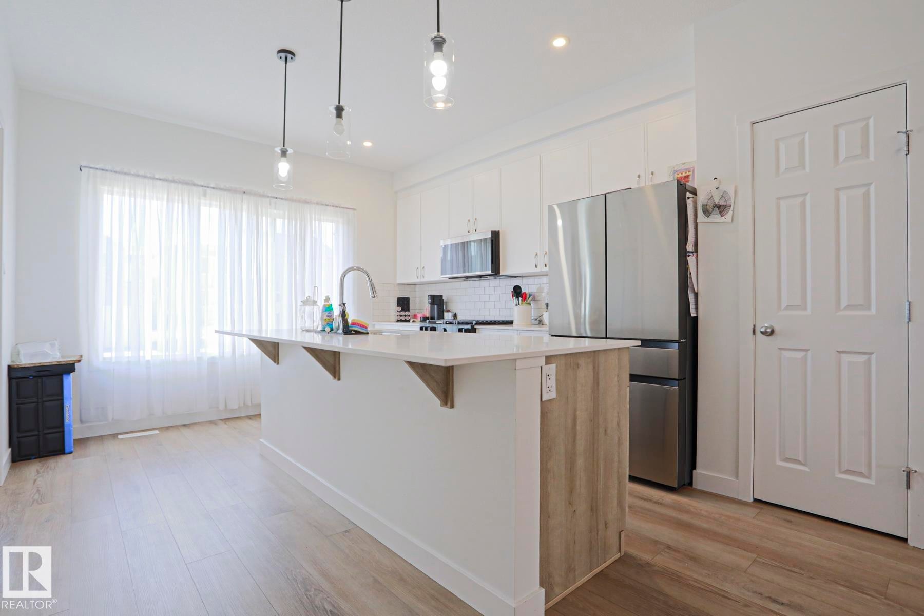 Kitchen featuring a central island with a quartz countertop, wood-finish paneling, and an undermount sink with a gooseneck faucet - 33 Eton Link, Spruce Grove, AB