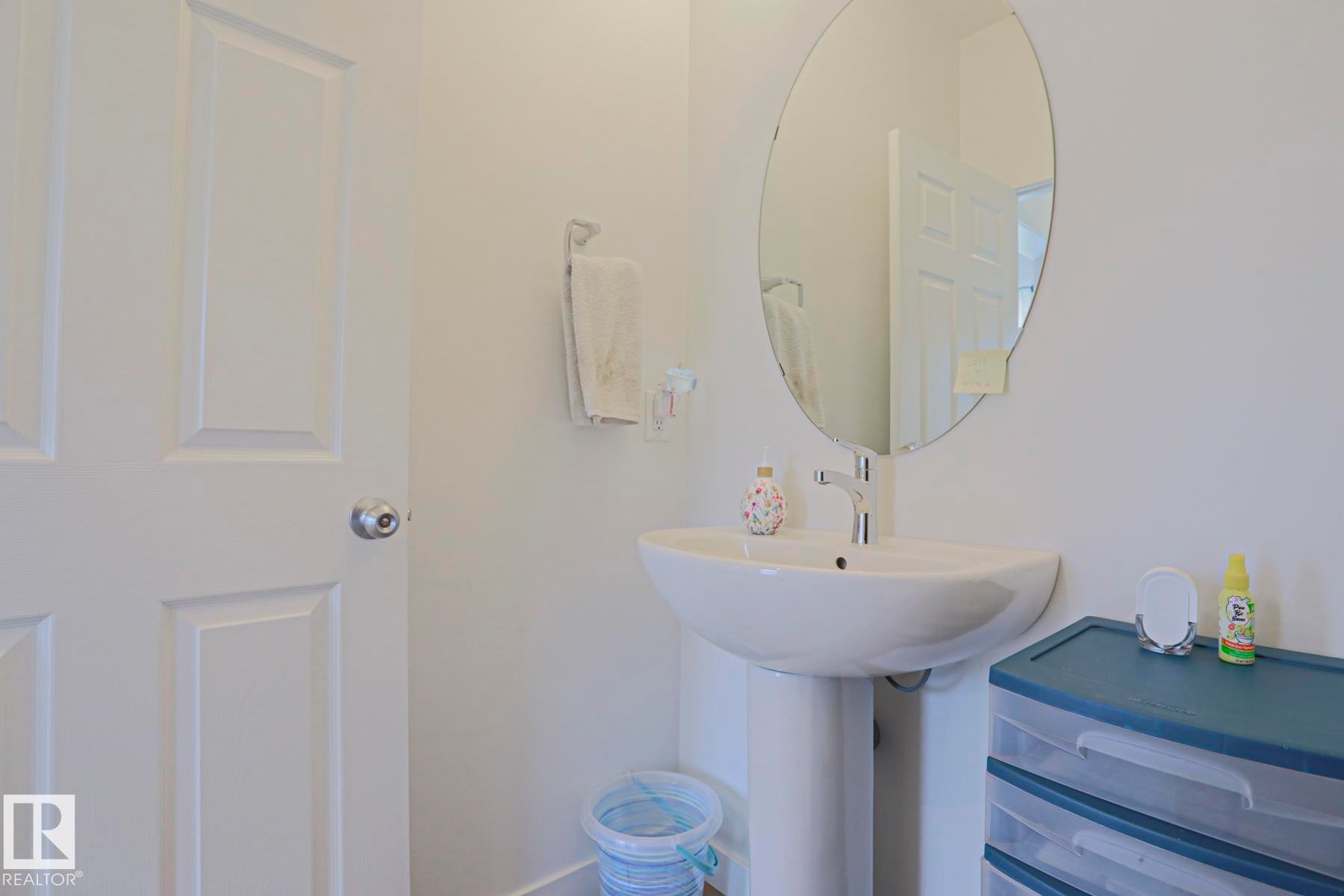 Pedestal sink with a polished chrome faucet, oval frameless mirror, and a panel interior door - 33 Eton Link, Spruce Grove, AB