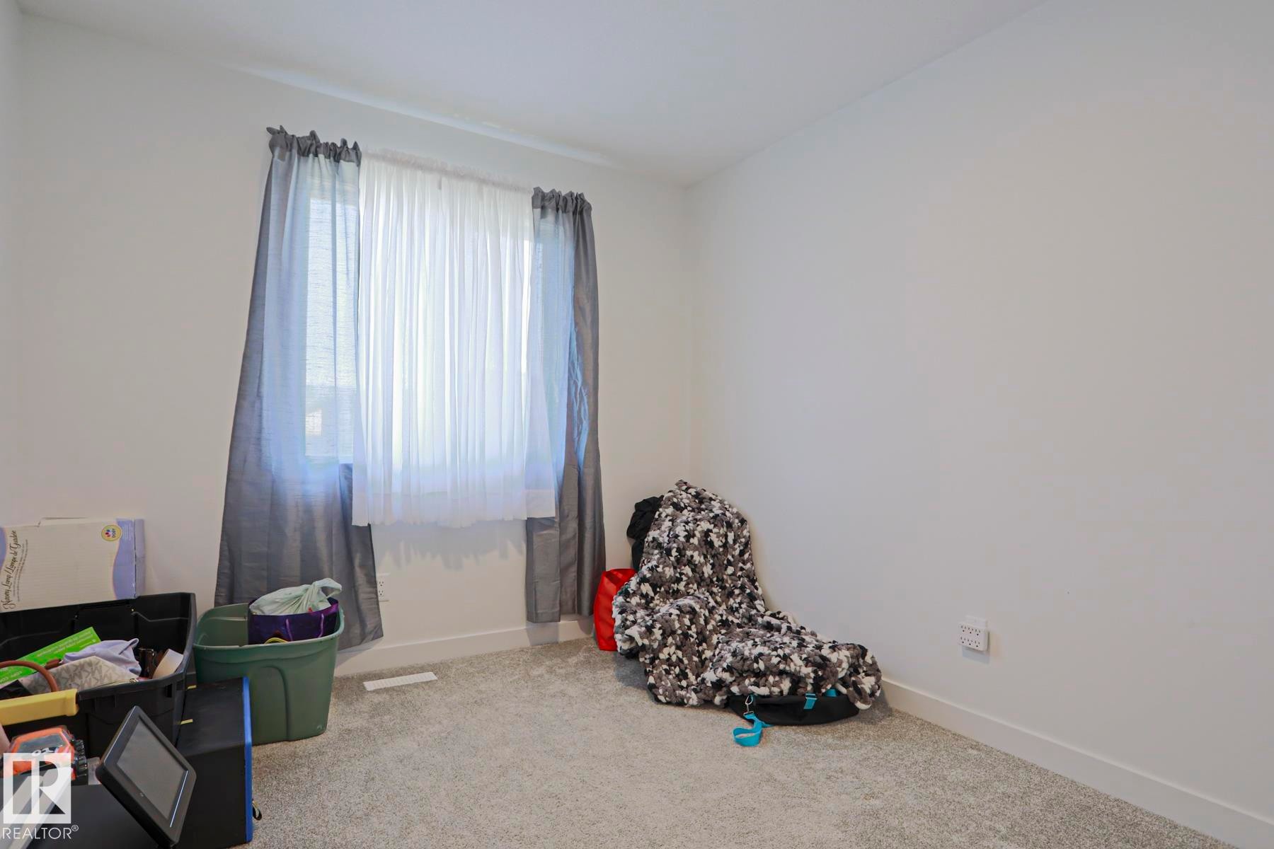 Carpeted room with a double window featuring sheer white and solid grey drapes - 33 Eton Link, Spruce Grove, AB