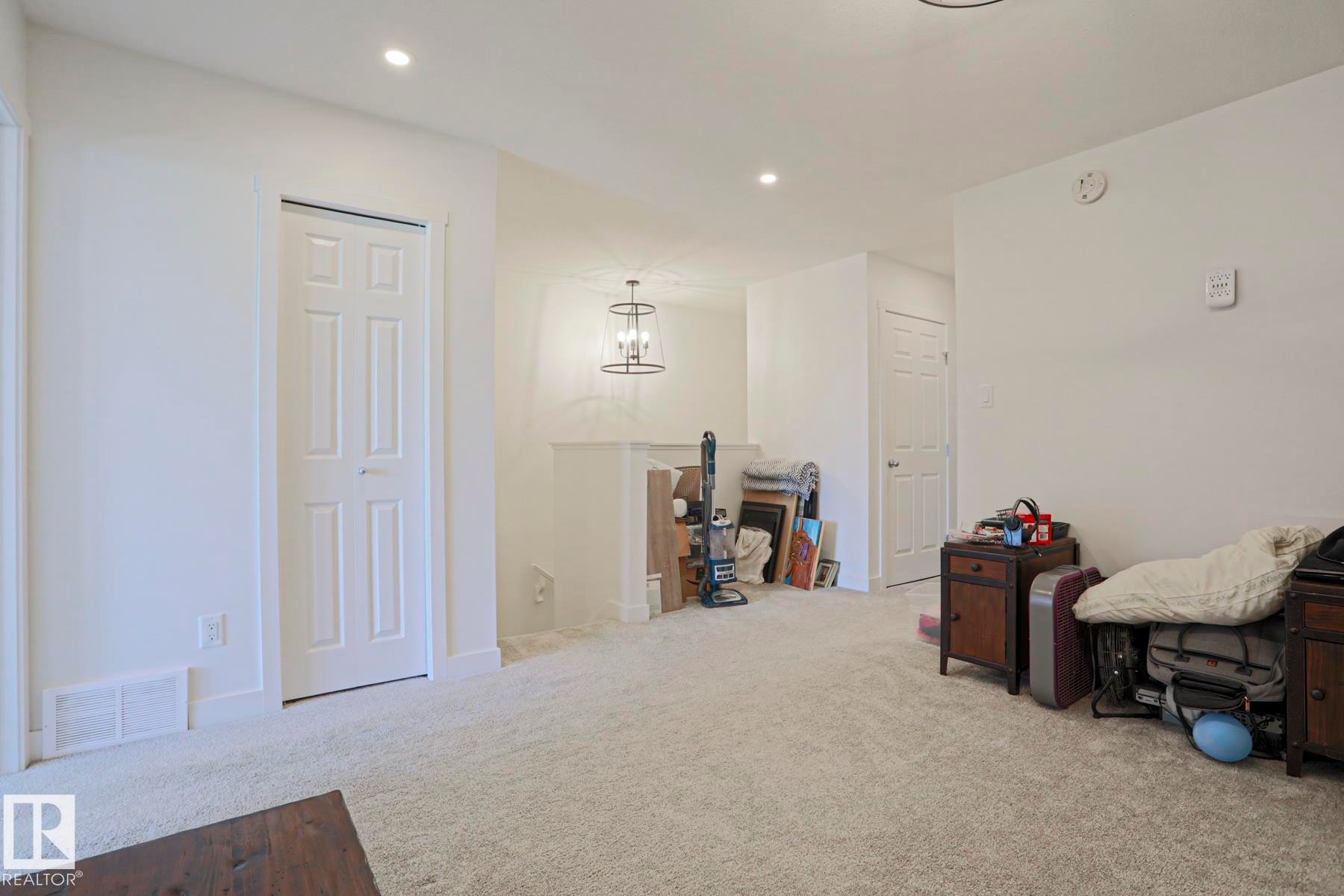 Carpeted interior area featuring white walls, recessed ceiling lighting, and a prominent chandelier with an open-cage design - 33 Eton Link, Spruce Grove, AB