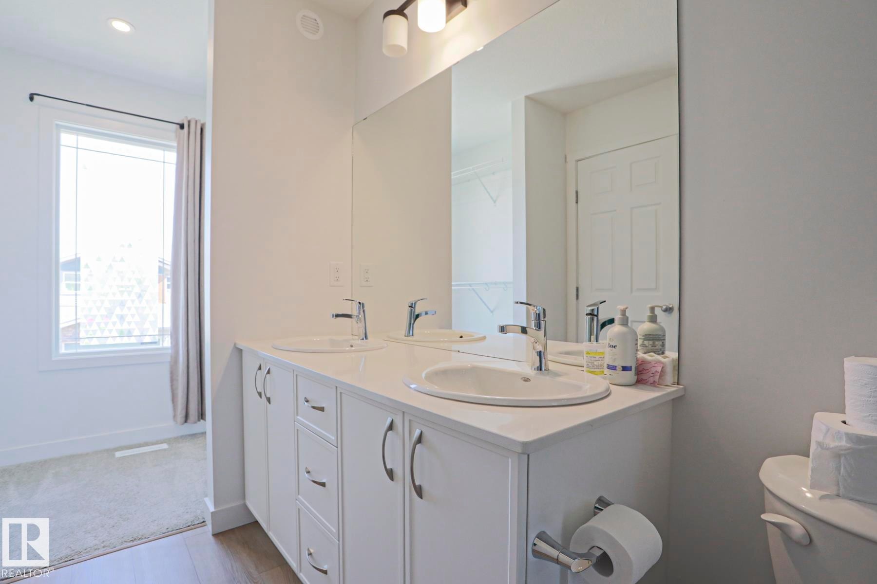 Dual vanity with white cabinetry, integrated sinks, chrome fixtures, and a large wall-mounted mirror - 33 Eton Link, Spruce Grove, AB