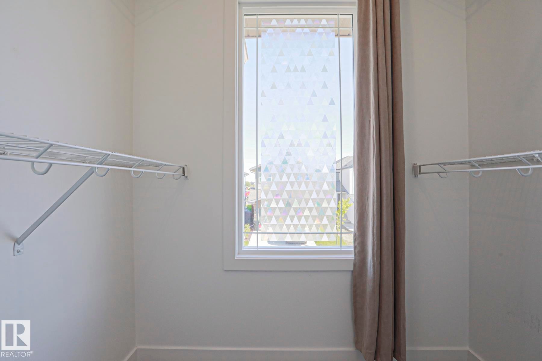 Closet space featuring white wire shelving, a window with patterned privacy film, and a neutral-toned curtain - 33 Eton Link, Spruce Grove, AB