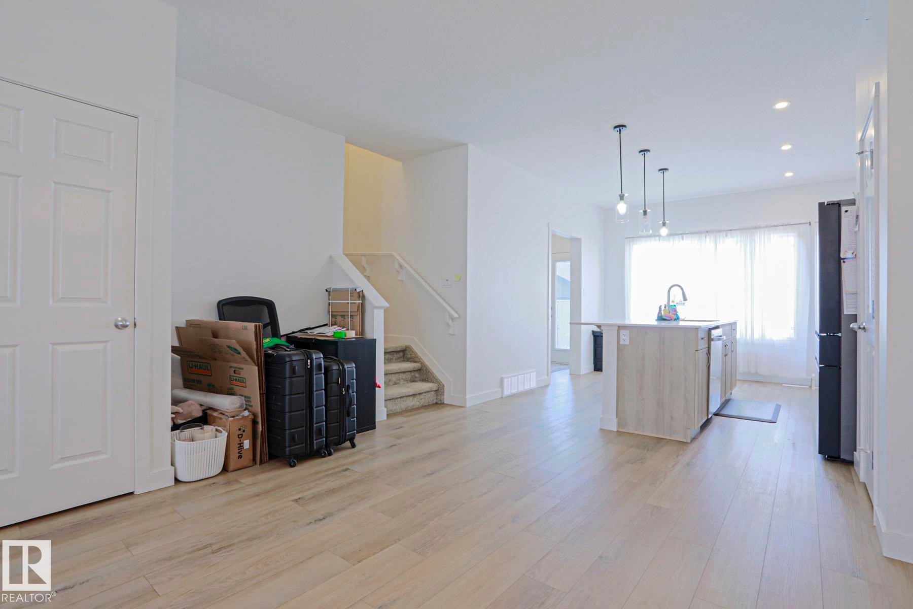 Open-concept living area featuring wood-finish flooring, a kitchen island with integrated sink, pendant lighting, and recessed ceiling lights - 33 Eton Link, Spruce Grove, AB