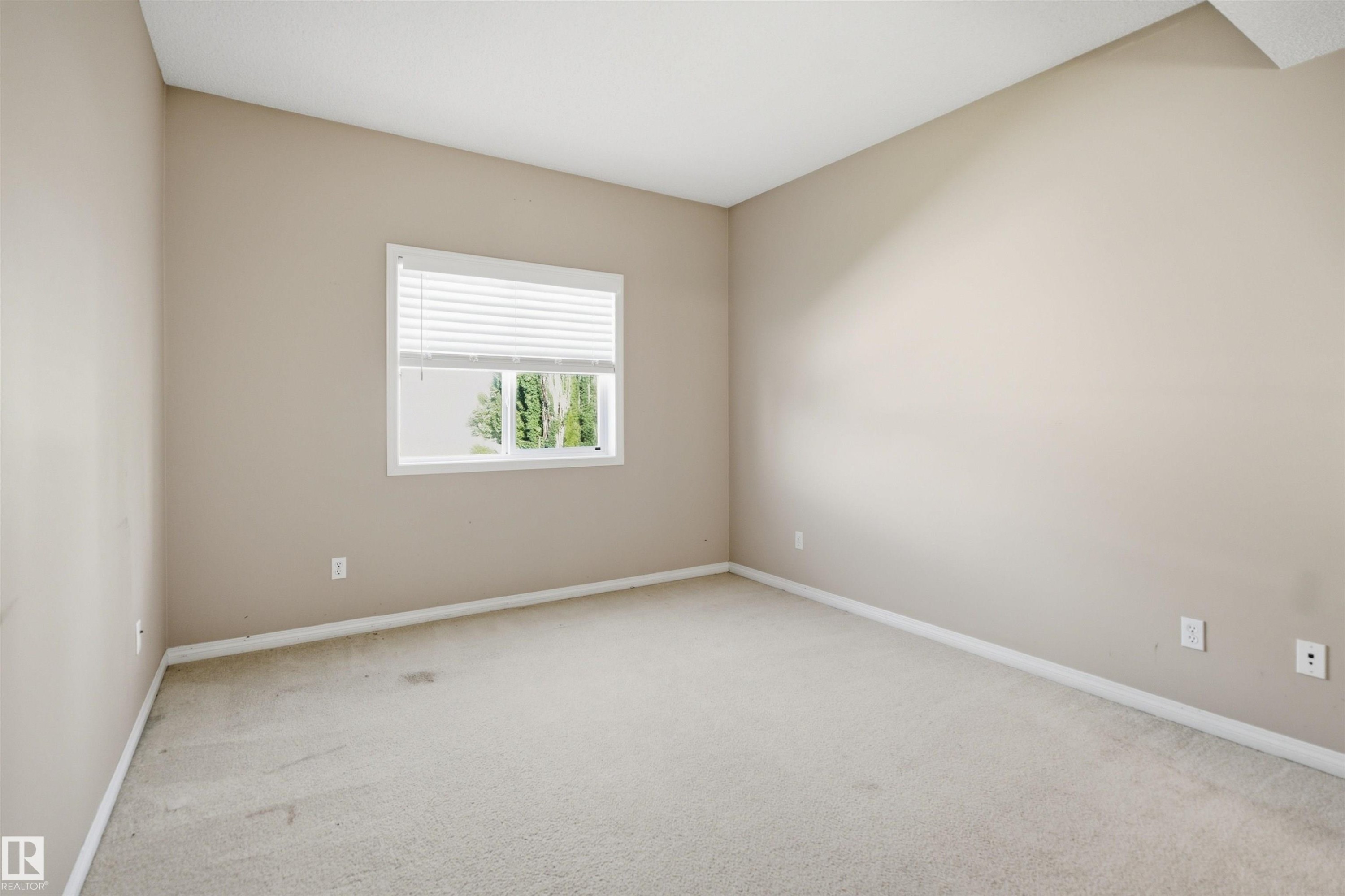 Spacious room featuring neutral painted walls, light-colored carpeting, and a white-framed window with blinds - 95 3040 Spence Wynd, Edmonton, AB