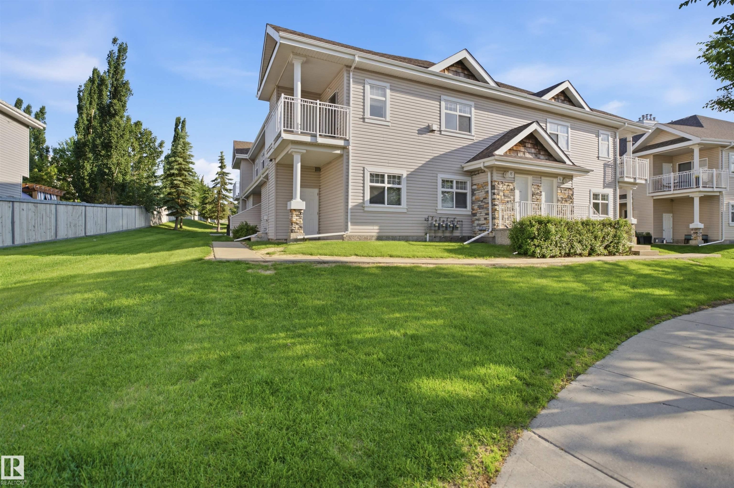 Multi-story exterior featuring neutral siding, stone accents, multiple balconies with white railings, a concrete pathway, and a surrounding green lawn - 95 3040 Spence Wynd, Edmonton, AB