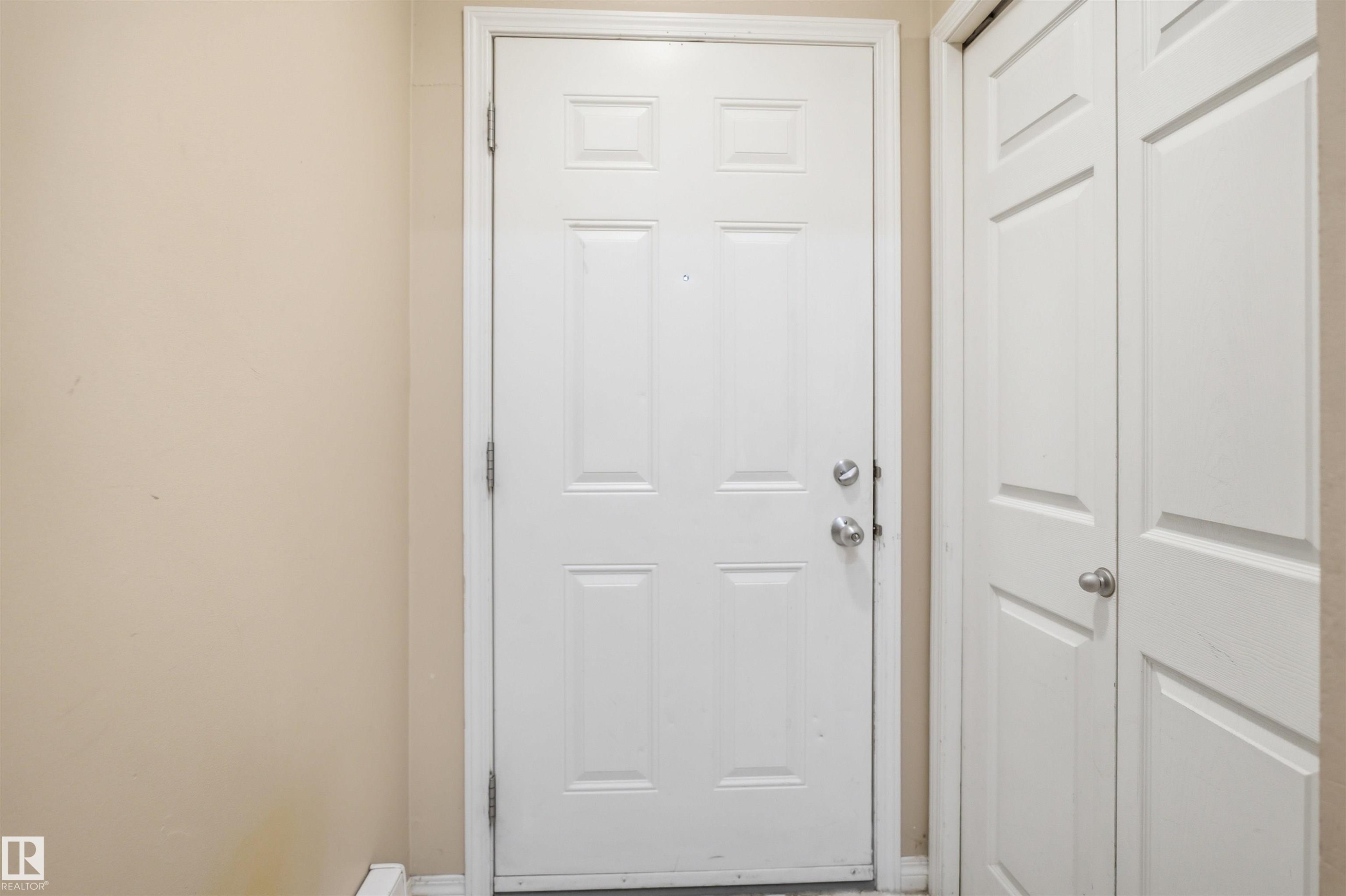 Panel-style entry door with chrome hardware, complemented by light beige wall paint and white trim - 95 3040 Spence Wynd, Edmonton, AB