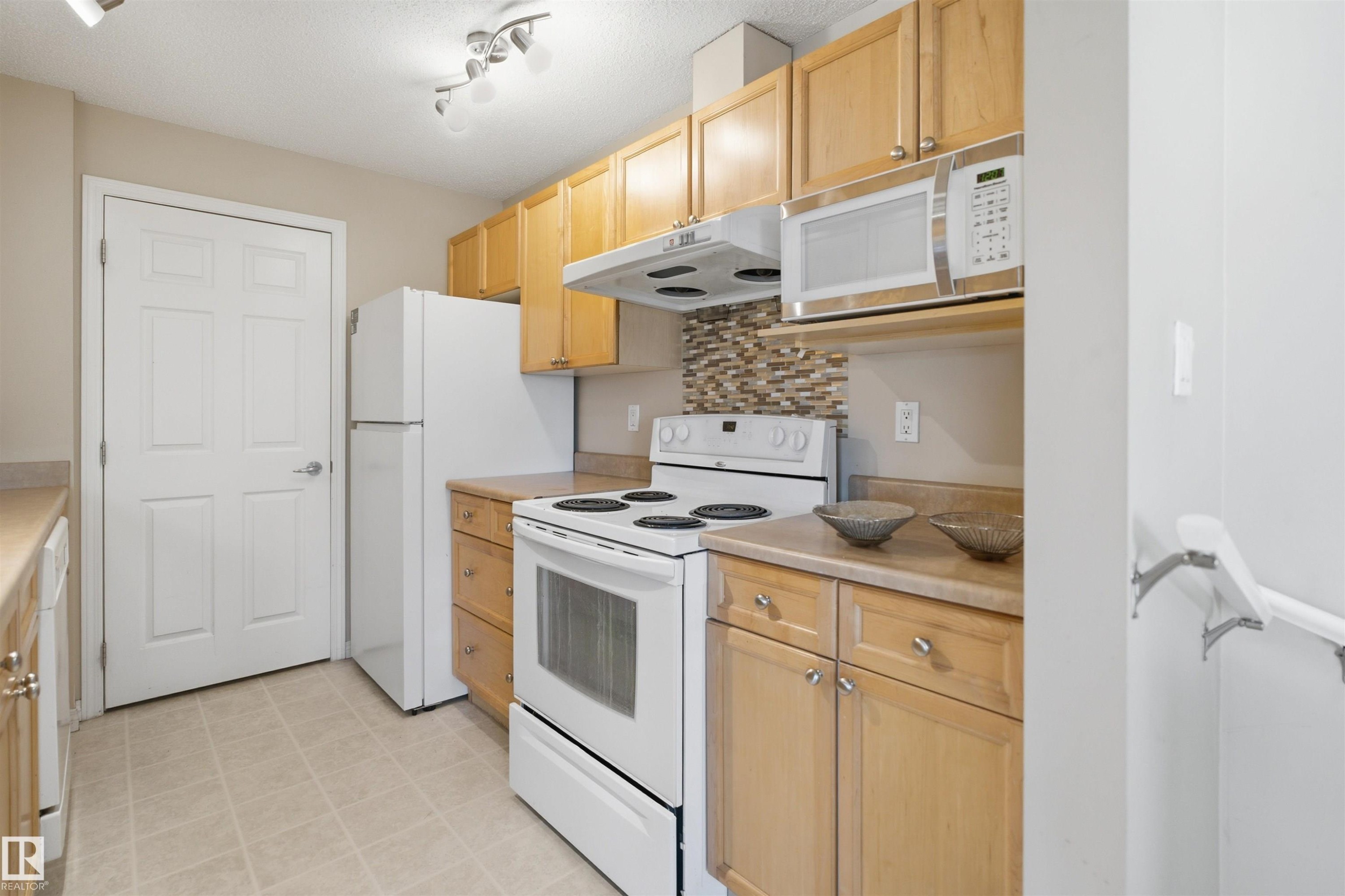 Kitchen featuring wood cabinetry, white appliances, a patterned tile backsplash, track lighting, and light-toned flooring - 95 3040 Spence Wynd, Edmonton, AB