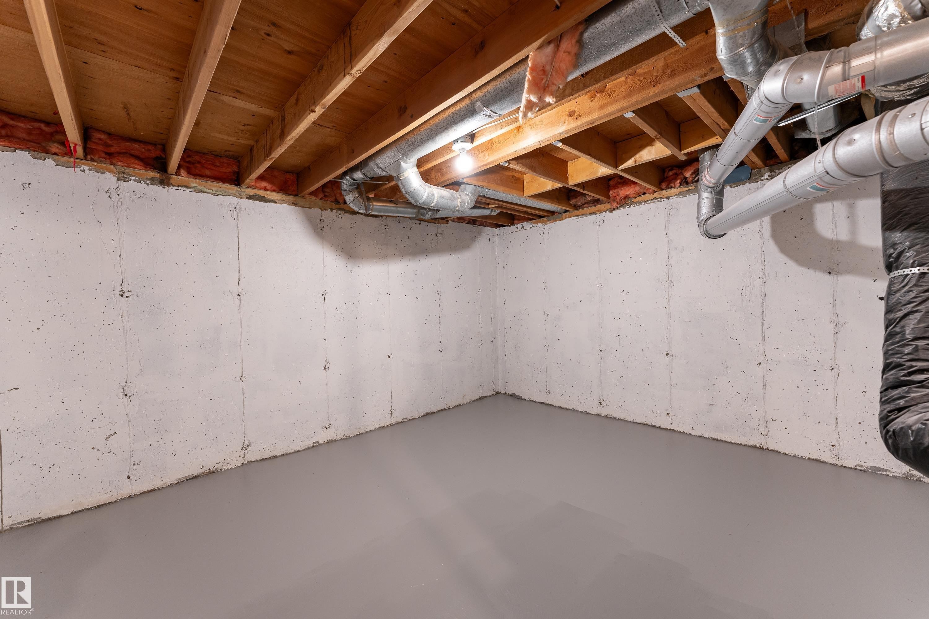 Unfinished basement space featuring exposed wood joists, concrete walls, and a gray painted concrete floor - 10 1415 62 Street, Edmonton, AB