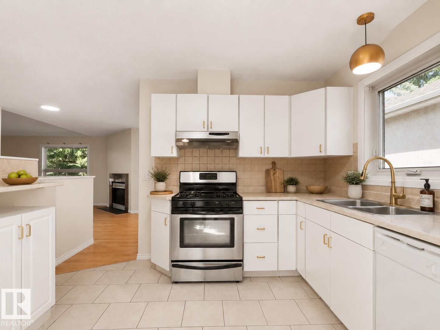 Kitchen featuring white cabinetry with gold-toned hardware, a stainless steel range with overhead ventilation, and a double basin sink with a gold-toned faucet - 1855 Mill Woods Rd E Nw, Edmonton, AB