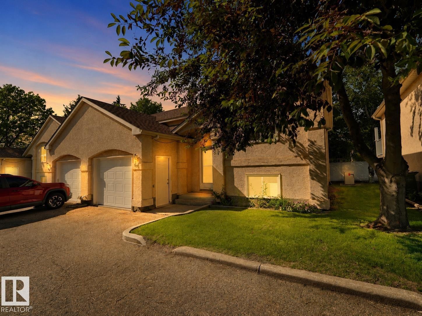 Stucco exterior residence featuring a two-car garage with arched entrances, a paved driveway, a landscaped lawn, and mature trees - 1855 Mill Woods Rd E Nw, Edmonton, AB