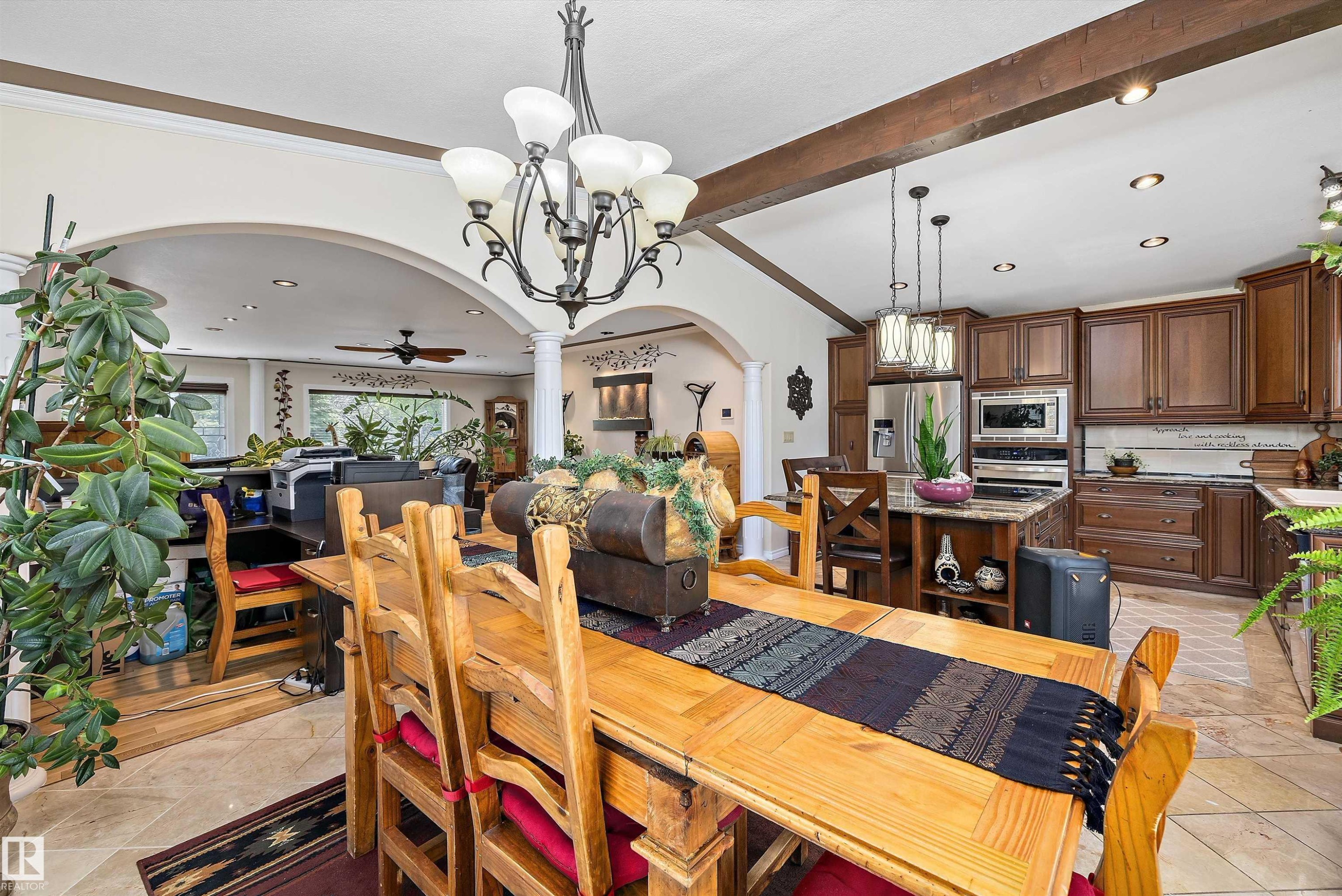 Open-concept living space featuring vaulted ceilings with exposed wood beams, a kitchen with wood cabinetry and stainless steel appliances, a central kitchen island with seating, a formal dining area, and archways leading to an additional living space - 11124 110A Avenue Nw, Edmonton, AB