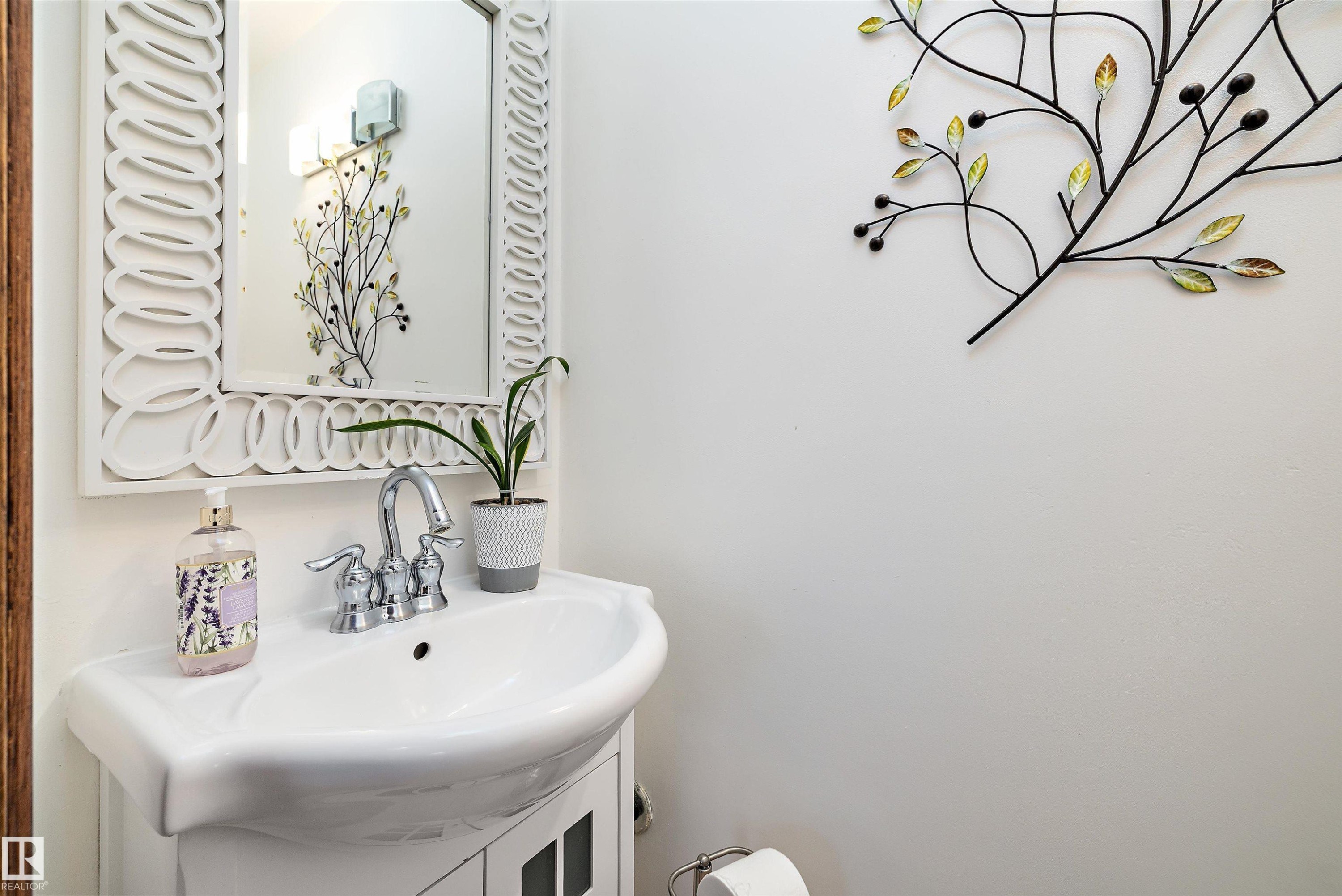 Pedestal sink with chrome faucet, framed by a decorative mirror and wall sconces - 11124 110A Avenue Nw, Edmonton, AB
