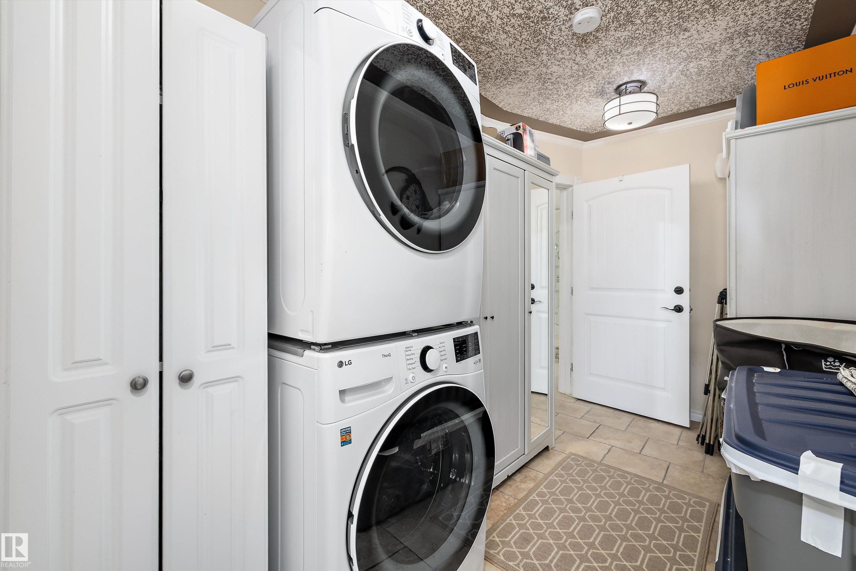 Dedicated laundry area featuring a stacked washer and dryer unit, bi-fold closet doors, a paneled door with dark hardware, tiled flooring, and a flush-mount ceiling light fixture - 11124 110A Avenue Nw, Edmonton, AB