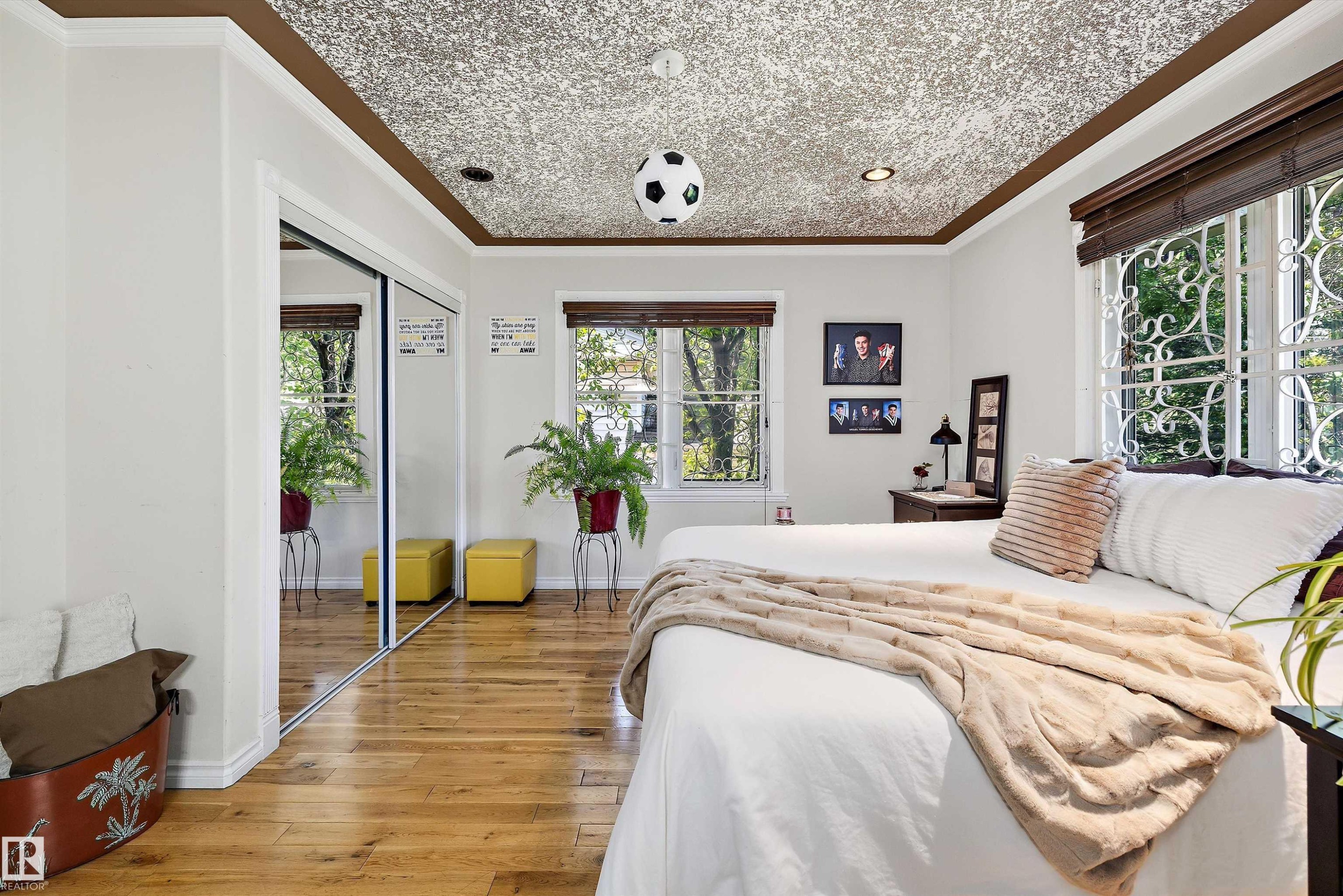 Room featuring wood-finish flooring, a decorative ceiling, dual windows with security bars, and mirrored sliding closet doors - 11124 110A Avenue Nw, Edmonton, AB