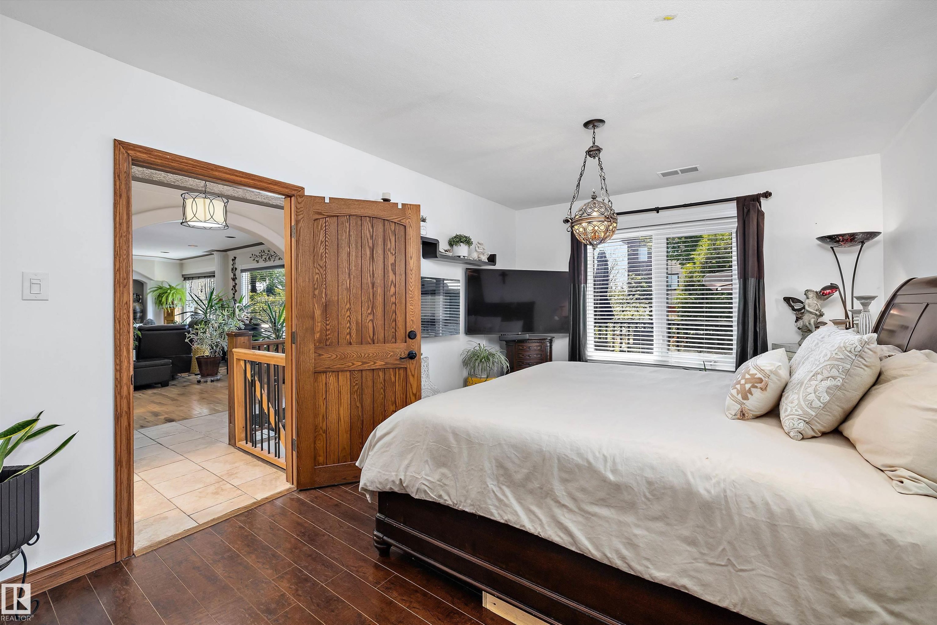 Bedroom featuring rich wood-finish flooring, a decorative overhead light fixture, and a window with horizontal blinds - 11124 110A Avenue Nw, Edmonton, AB