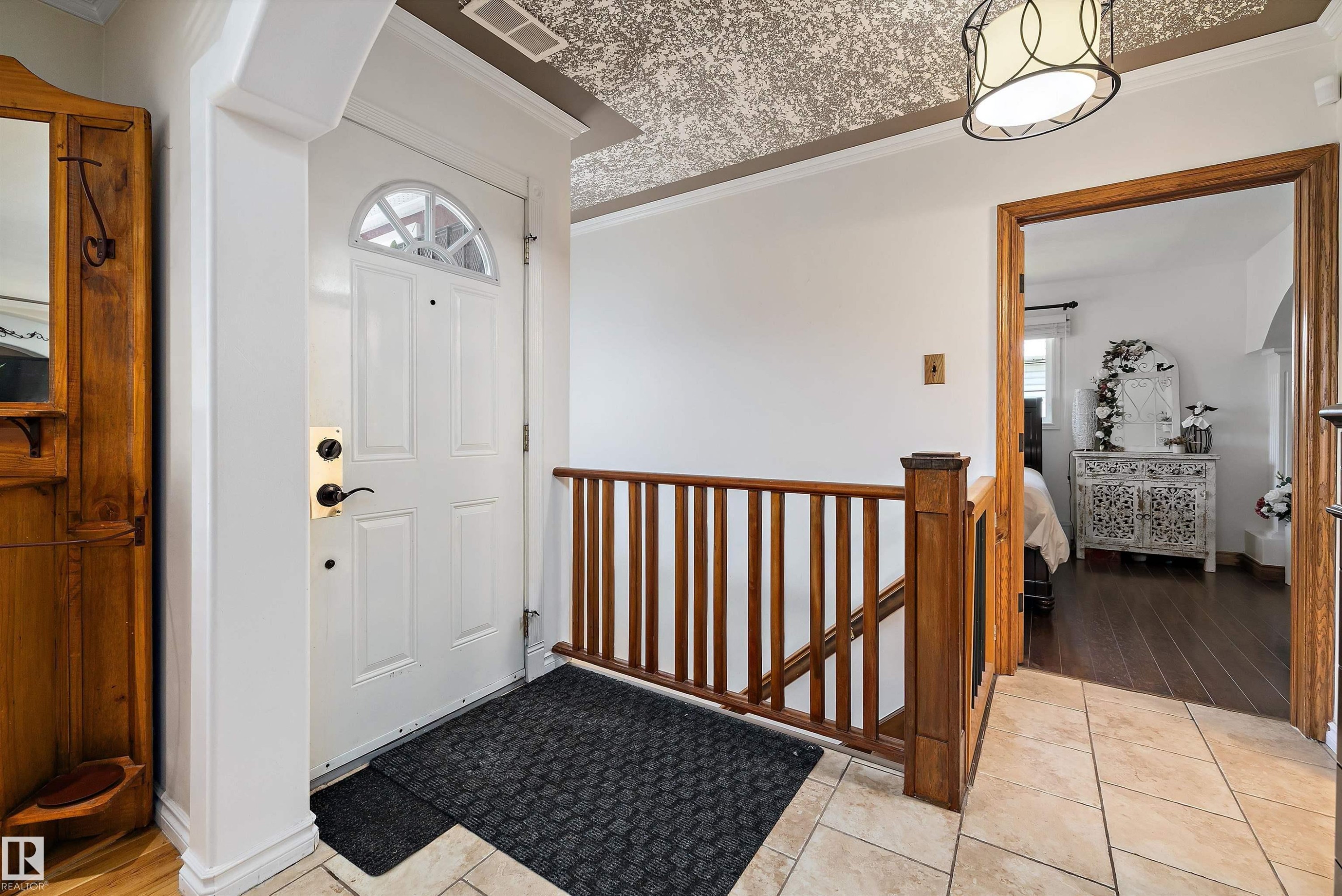 Entryway featuring a white paneled door with an arched window, a wood-finish staircase railing, and tile flooring - 11124 110A Avenue Nw, Edmonton, AB