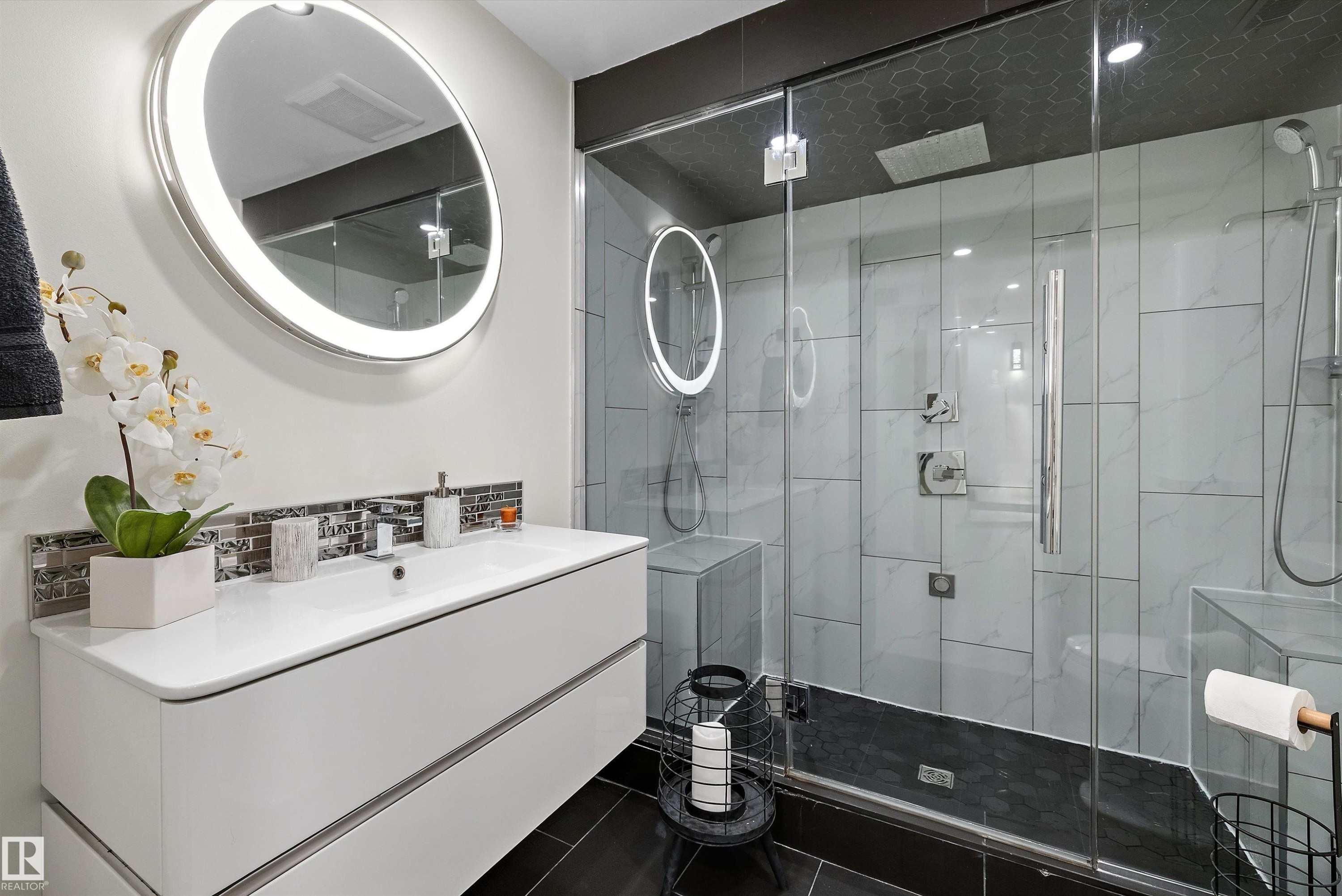 Contemporary bathroom featuring a floating white vanity with integrated sink, an illuminated circular mirror, and a glass-enclosed shower - 11124 110A Avenue Nw, Edmonton, AB