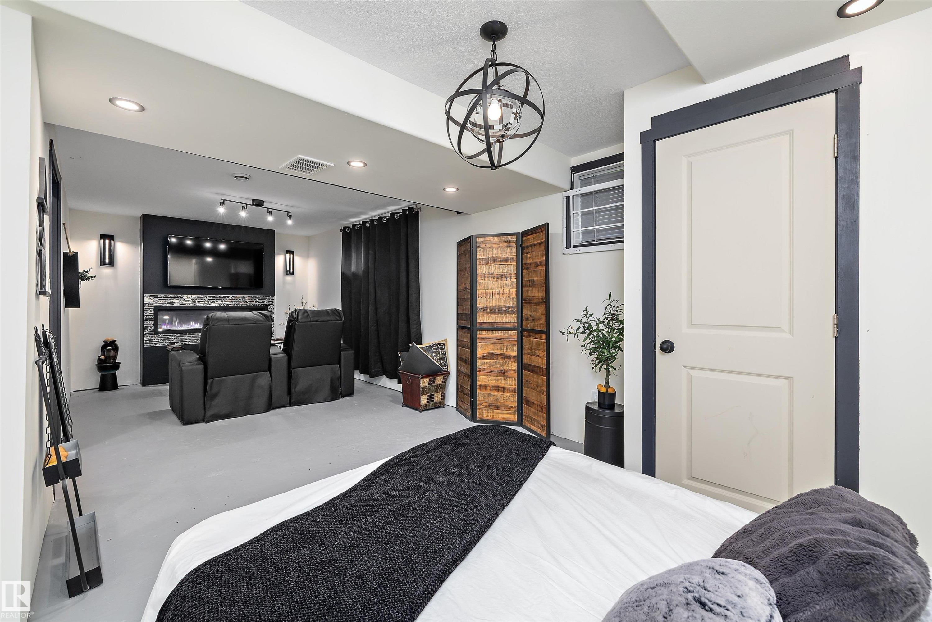 Finished lower level featuring recessed lighting, a built-in electric fireplace with stone-look surround, a wall-mounted television area, and a decorative orb chandelier - 11124 110A Avenue Nw, Edmonton, AB