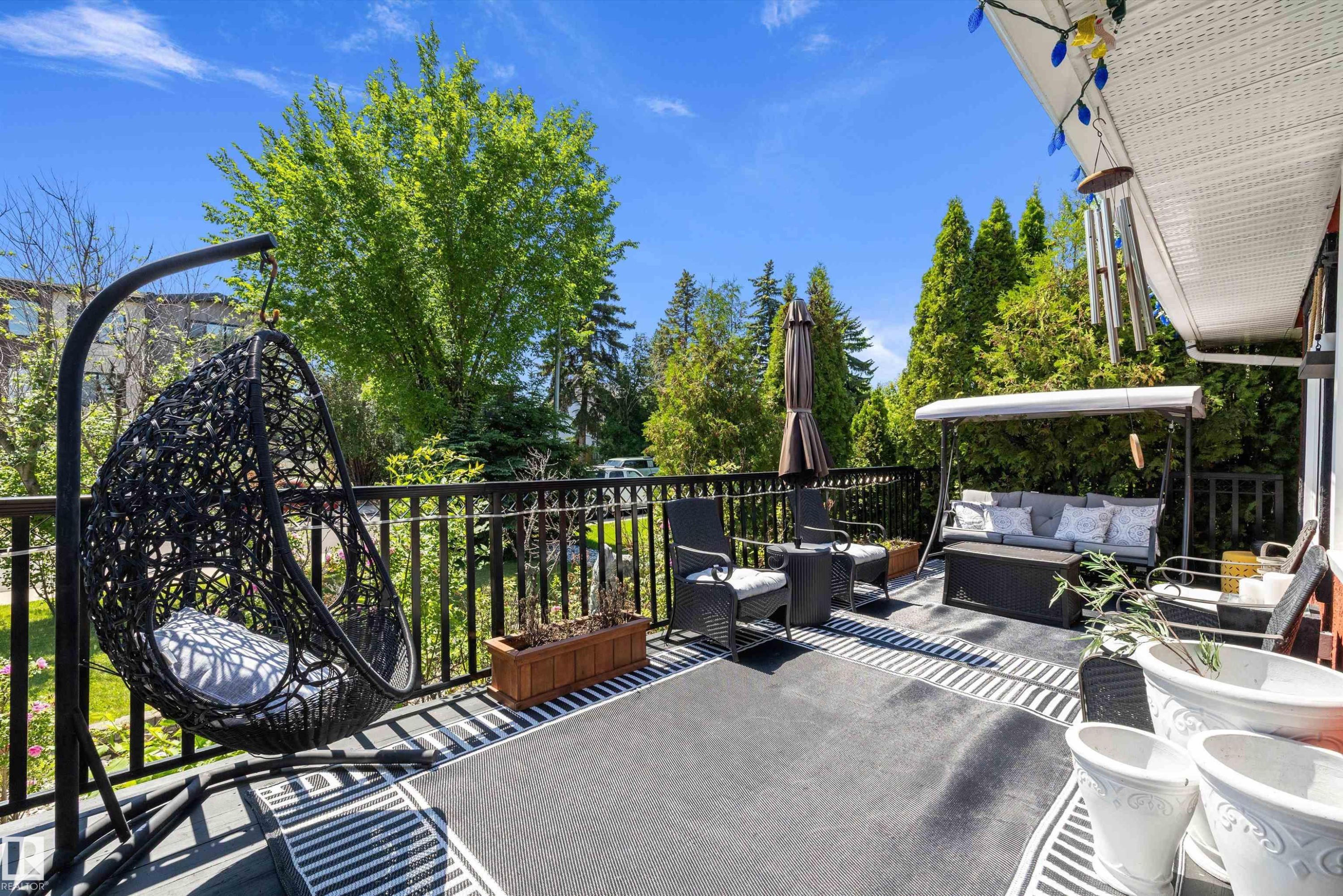 Spacious outdoor deck featuring a dark gray striped area rug, black metal railings, and mature surrounding trees - 11124 110A Avenue Nw, Edmonton, AB