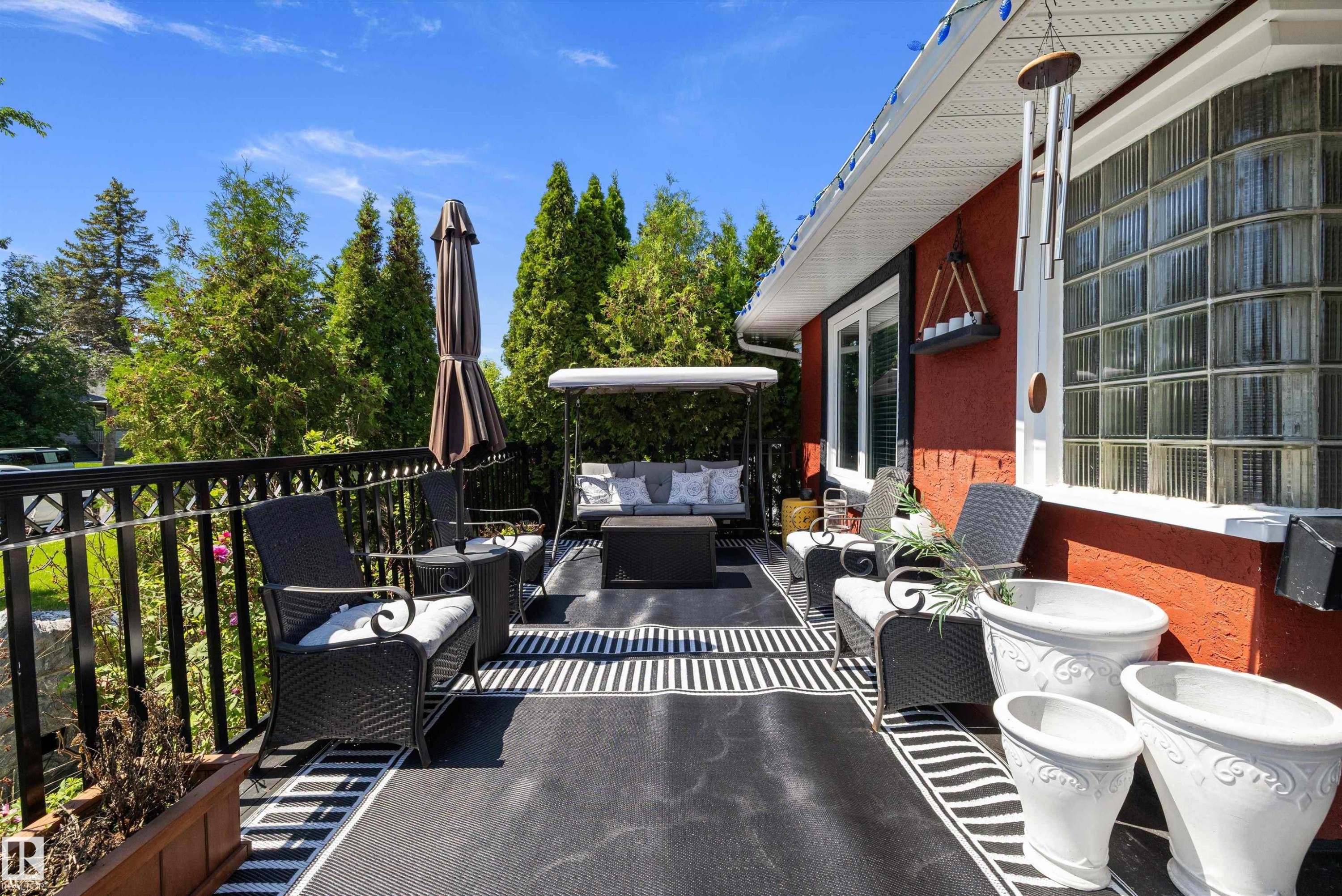 Expansive outdoor patio featuring a black metal railing, patterned outdoor rugs, and a red exterior wall - 11124 110A Avenue Nw, Edmonton, AB
