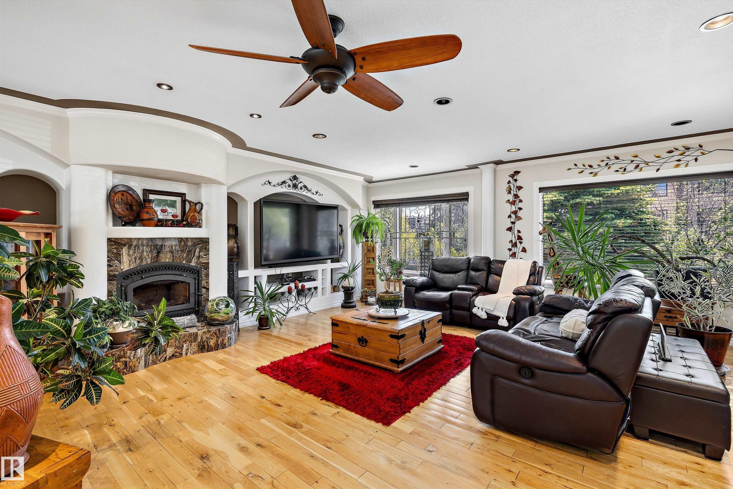 Spacious living area featuring light wood-finish flooring, a wood-burning fireplace with a stone surround, recessed lighting, and a ceiling fan - 11124 110A Avenue Nw, Edmonton, AB